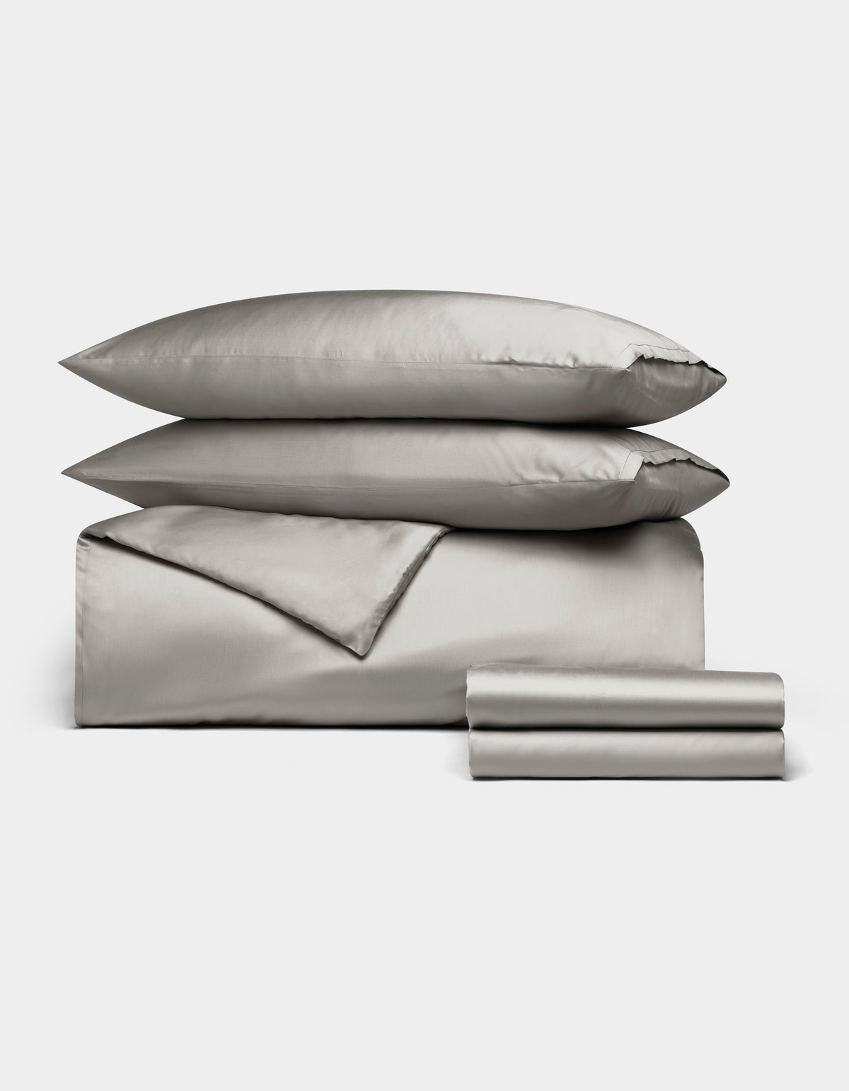The Cozy Earth Bamboo Bedding Deluxe Bundle features light gray satin bedding with two pillows, a folded duvet, and stacked sheets, all neatly arranged on a white background.