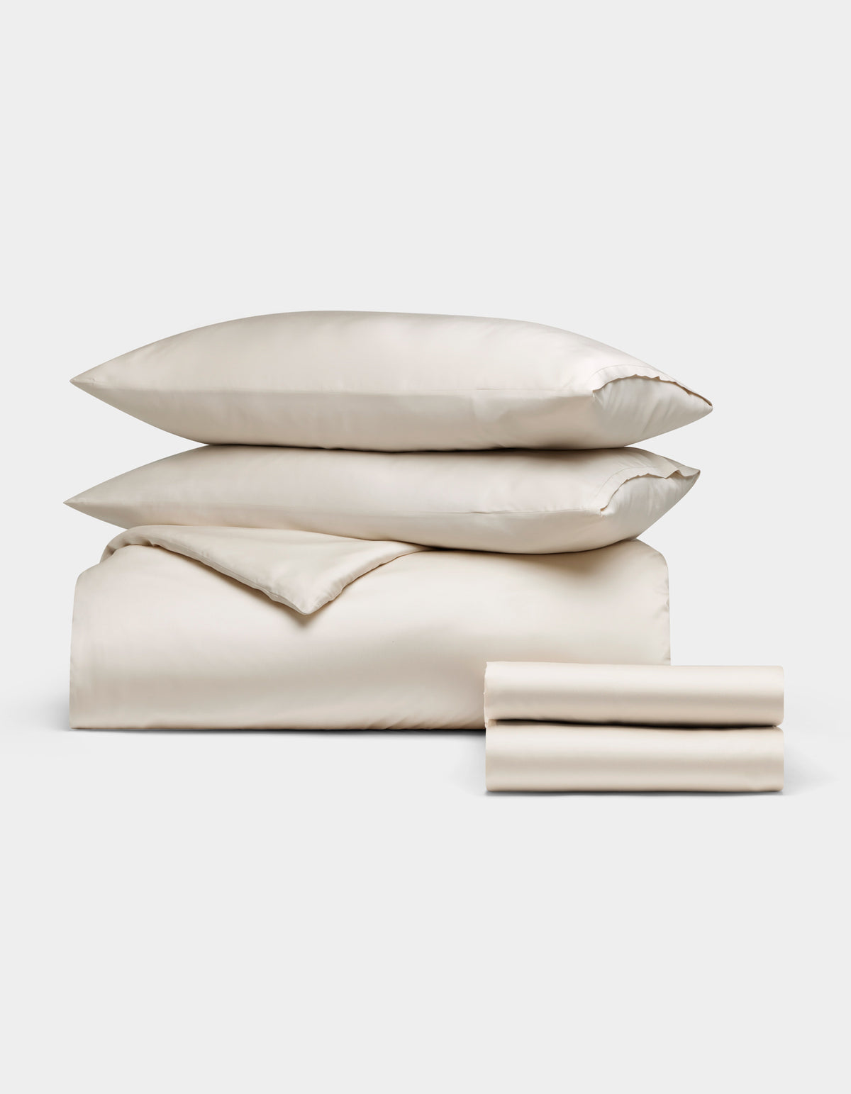 Cozy Earth's Bamboo Bedding Deluxe Bundle, featuring two pillows, a folded comforter, and two folded sheets in cream, is neatly stacked and displayed on a plain white background.|Color:Oat