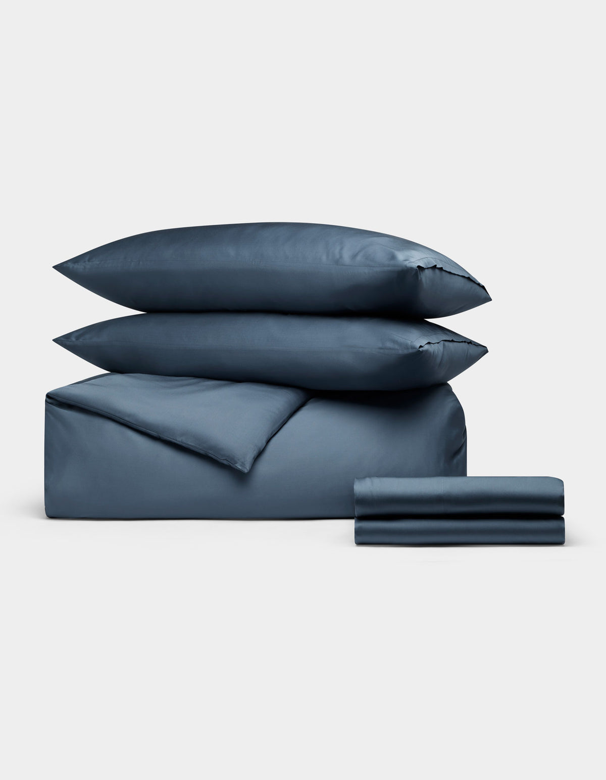 The Cozy Earth Bamboo Bedding Deluxe Bundle, featuring two pillows, a comforter, and folded sheets in blue, is neatly stacked against a plain light gray background.|Color:Pacific Blue