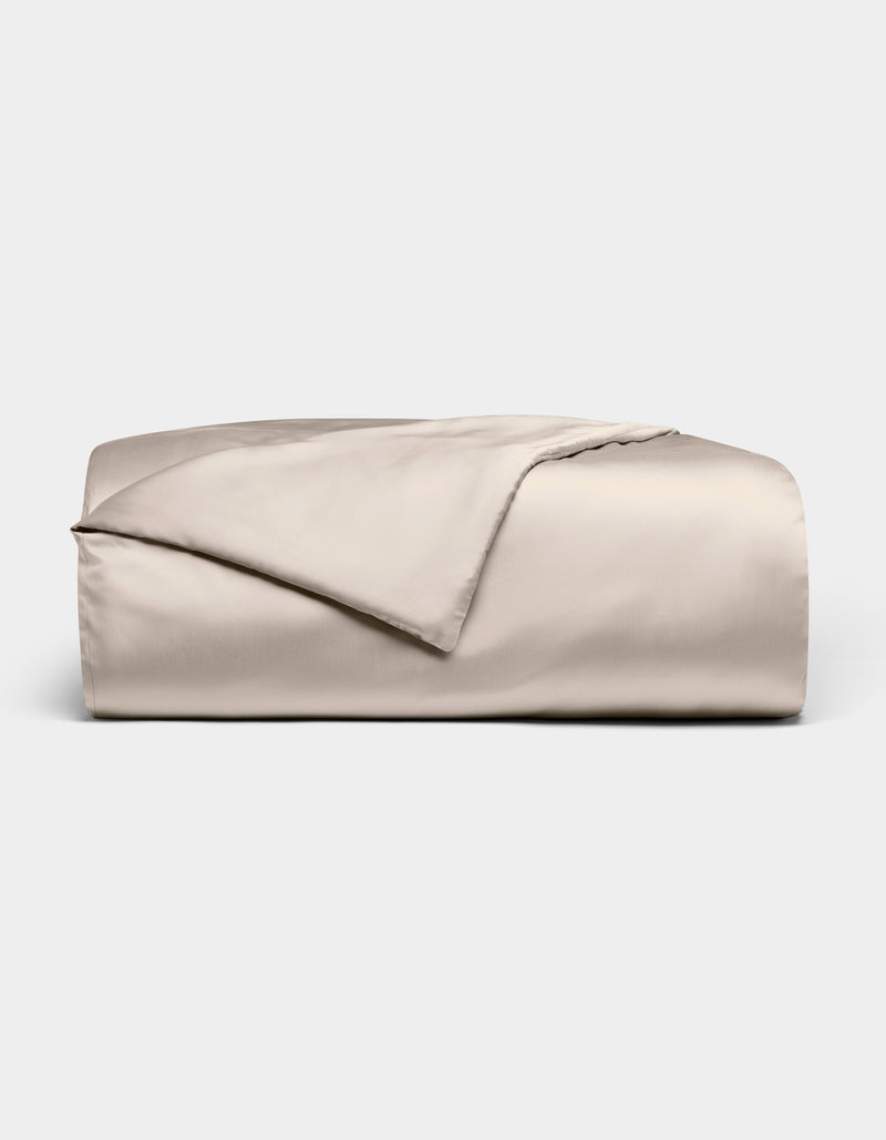 The Bamboo Duvet Cover by Cozy Earth is shown neatly folded in light beige with a smooth, shiny finish against a white background; one corner is flipped open to reveal the inner side.