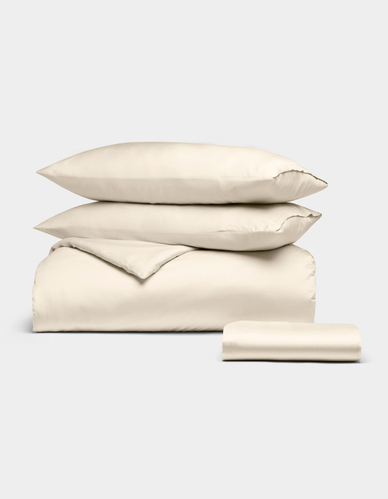 The Cozy Earth Bamboo Bedding Essential Bundle, featuring a cream-colored duvet cover, two pillowcases, and a flat sheet, is neatly folded and displayed against a plain white background.