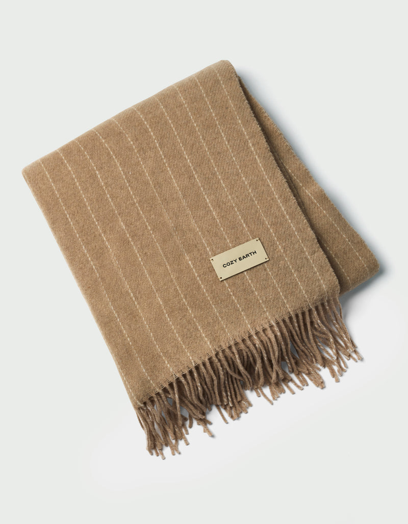 The Florence Throw by Cozy Earth is a tan, folded blanket with white pinstripes, fringed edges, and a rectangular "COZY EARTH" label on top, shown against a white background.