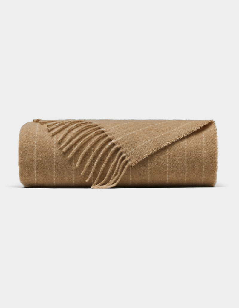 The Florence Throw by Cozy Earth is a light brown wool blanket with subtle white stripes and fringed edges, shown against a plain white background.