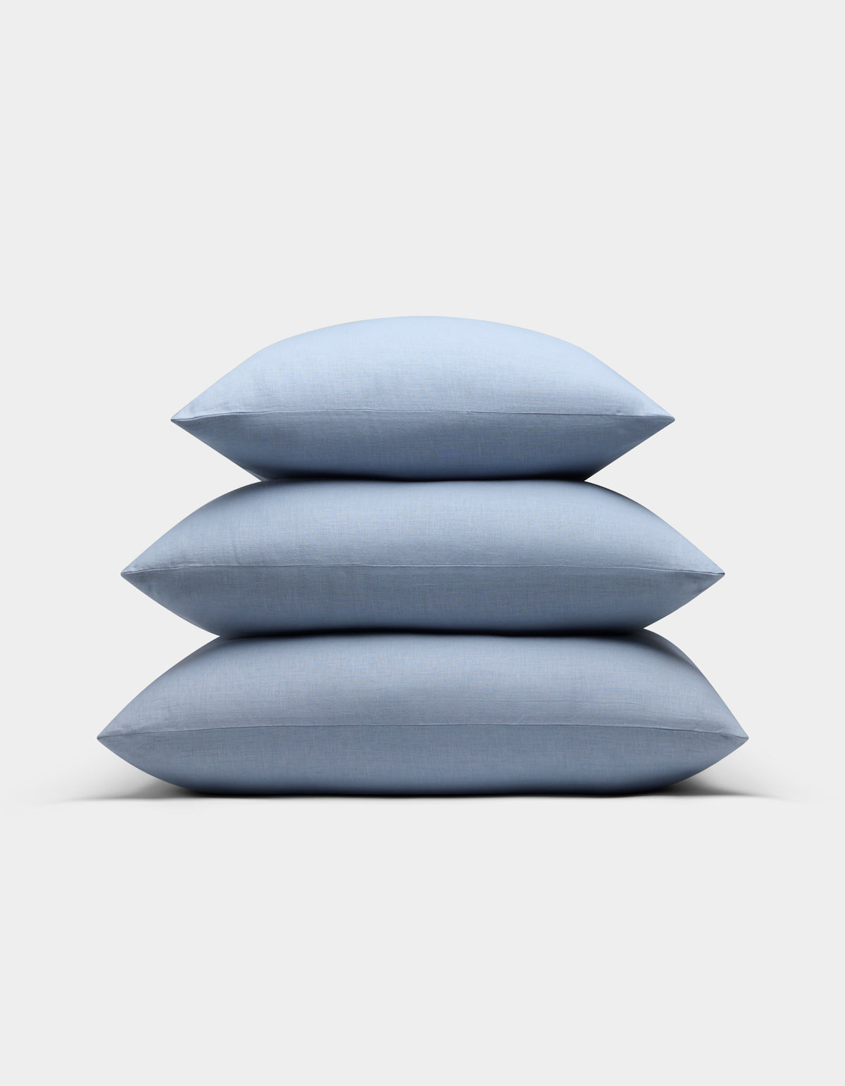 Three Cozy Earth Linen Throw Pillows in light blue are stacked neatly on top of each other against a plain white background.