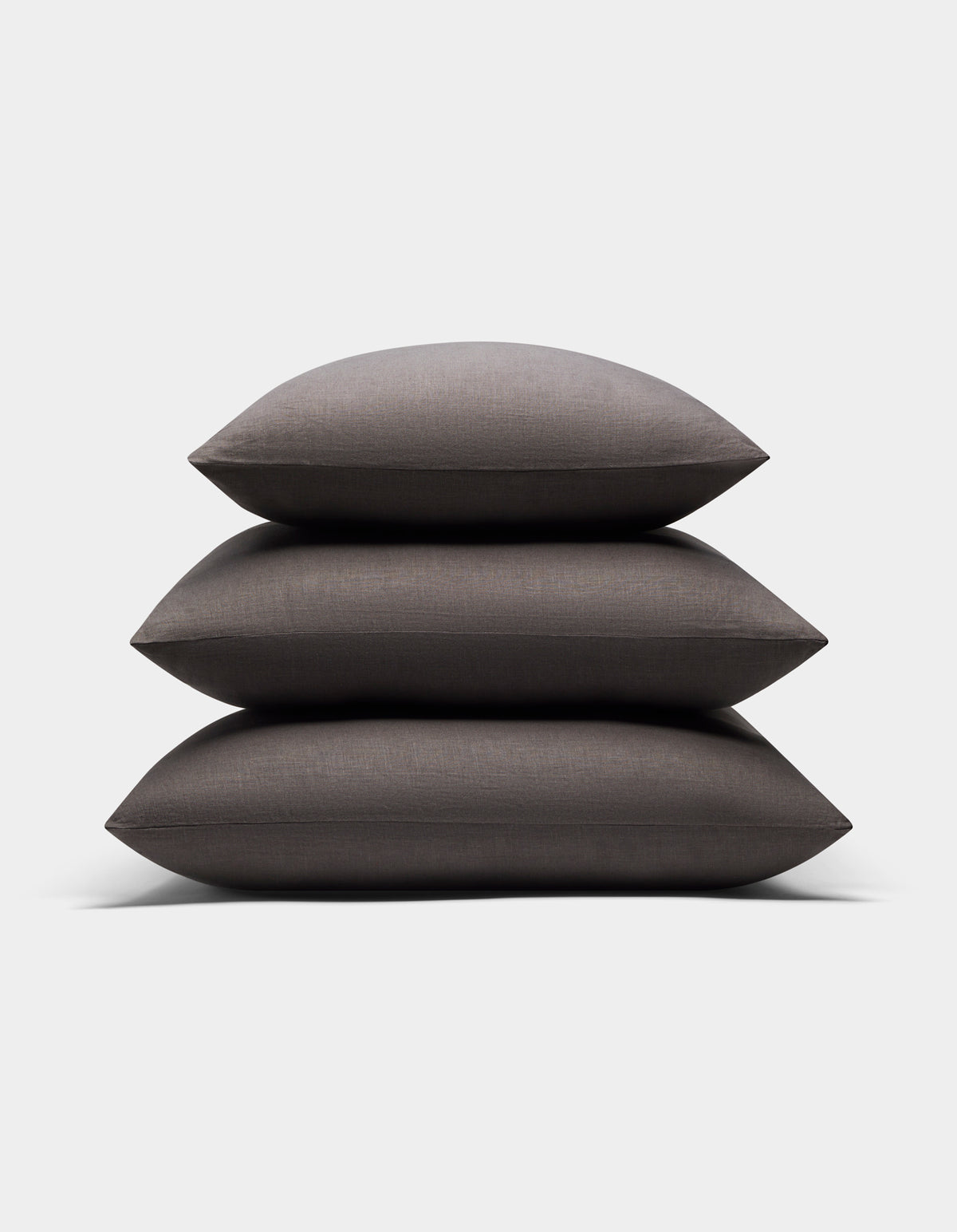 Three Cozy Earth Linen Throw Pillows in dark gray are neatly stacked together against a plain white background.