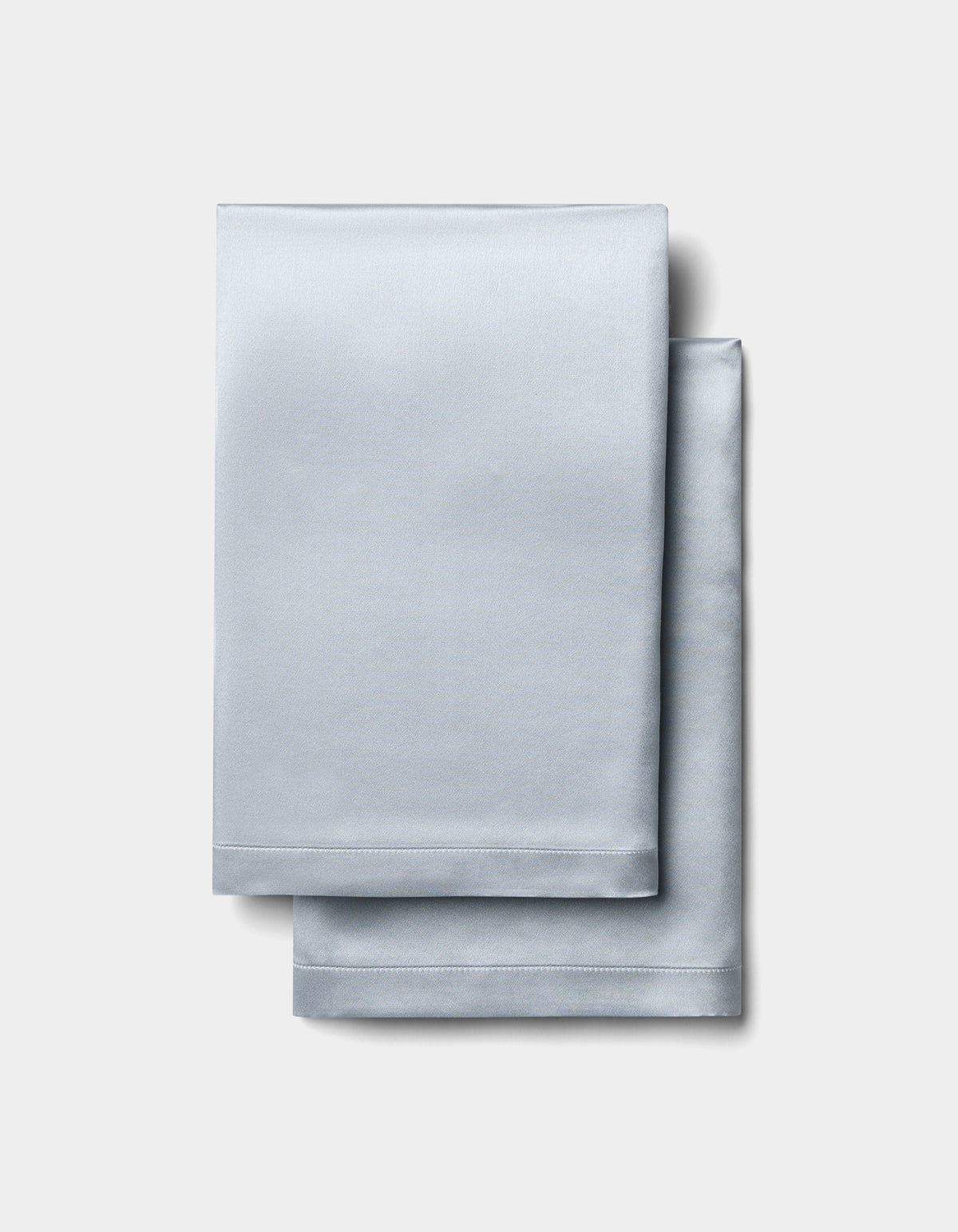 Two neatly folded Cozy Earth Silk Pillowcases are stacked on a plain, light gray background. |Color:Shore