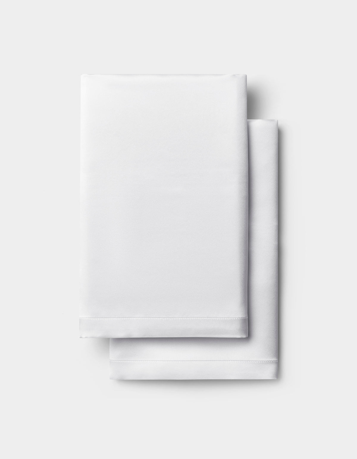 A neatly folded white Silk Pillowcase by Cozy Earth is stacked on a light gray background.