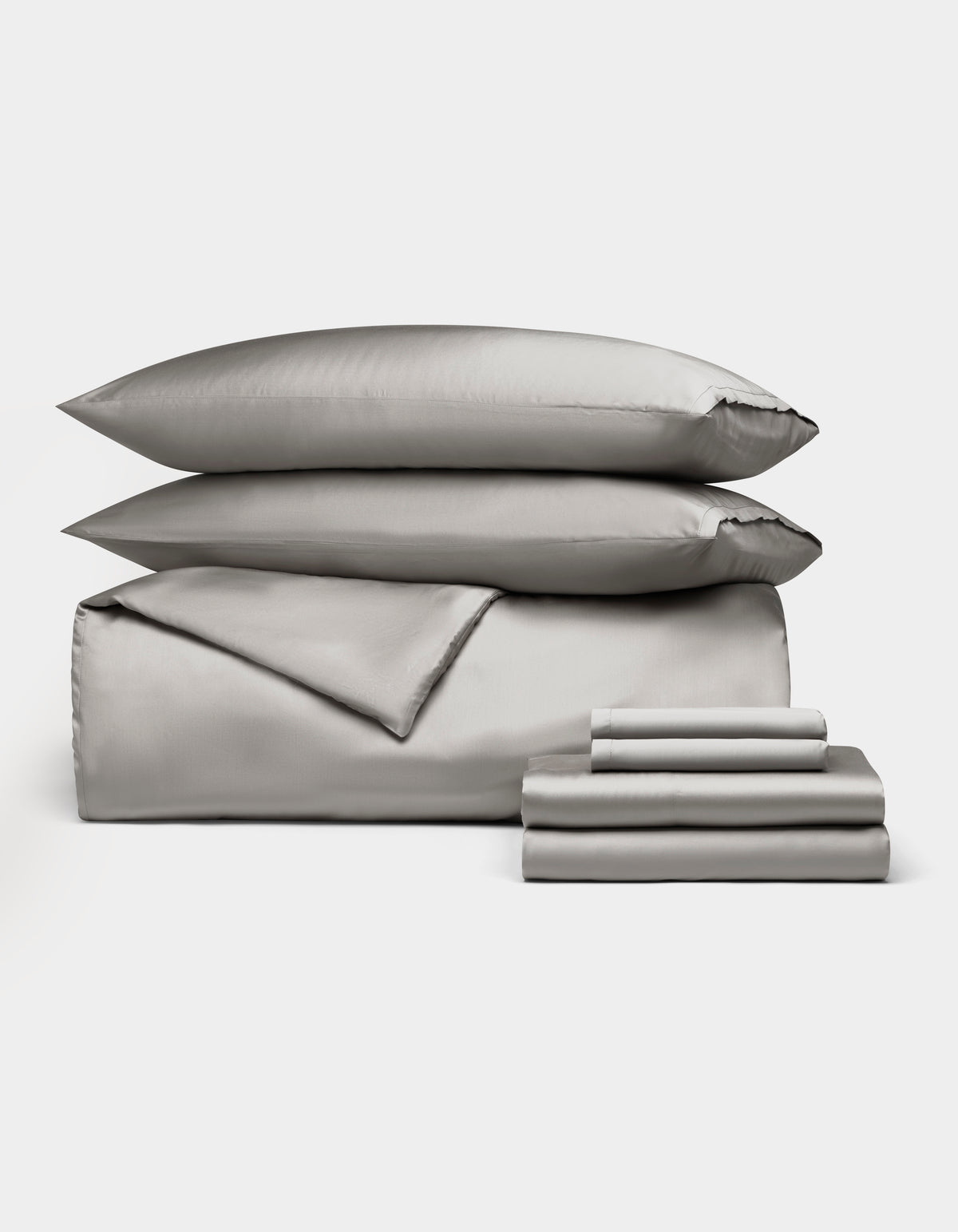 The Bamboo Bedding Ultimate Bundle by Cozy Earth features elegant silver-gray bedding, including two pillows, a comforter, and folded sheets, all neatly displayed against a plain white background.|Color:Light Grey