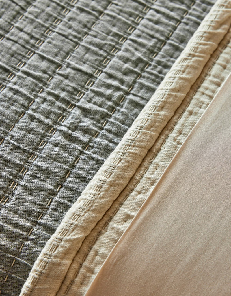 Close-up of the Cozy Earth Baja Matelasse Coverlet, featuring a stitched geometric texture, cream border, and smooth light beige fabric alongside.