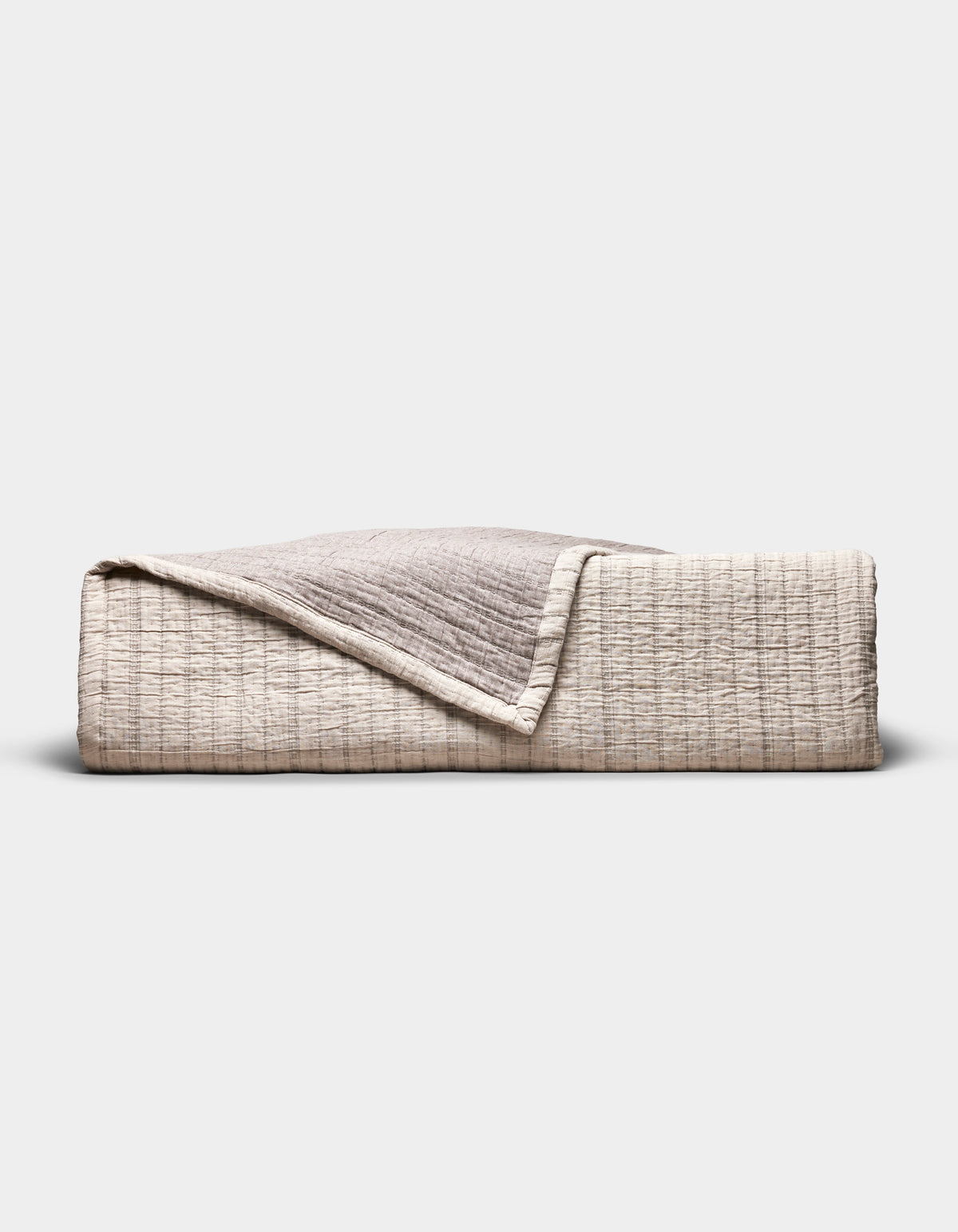 The Cozy Earth Baja Matelasse Coverlet, folded to display its textured beige and light brown fabric with one corner turned down, is pictured against a plain white background.|Color:Ebony/Taupe