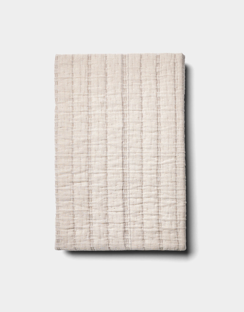 The Cozy Earth Baja Matelasse Sham, featuring a cream color and subtle grid texture, is neatly folded and displayed on a plain light background.