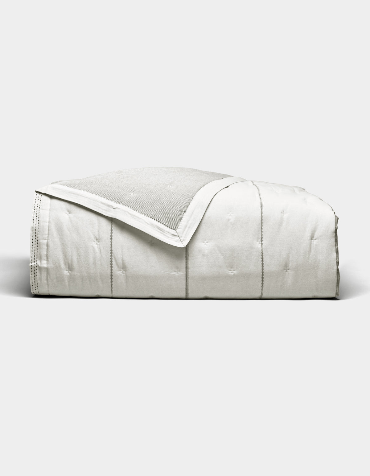 The Cozy Earth Baja Quilt, featuring stitched detailing, is neatly folded and displayed against a plain light gray background.