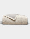 The Cozy Earth Baja Quilt, featuring a cream color with visible stitching and a light gray underside, is neatly folded and set against a plain white background.|Color:Coal Stripe/Striped Alabaster