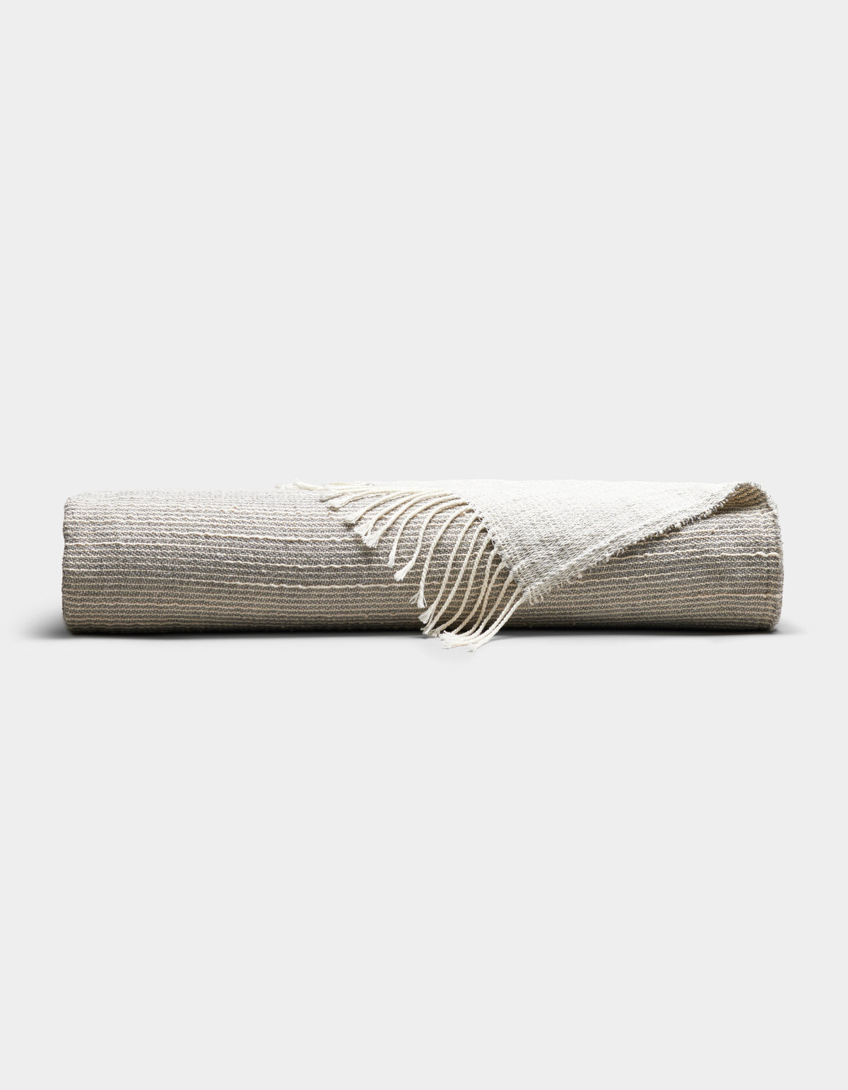 The Cozy Earth Baja Tassel Throw, a striped blanket in neutral beige and off-white tones with fringed edges, is neatly rolled and displayed on a plain, light background.