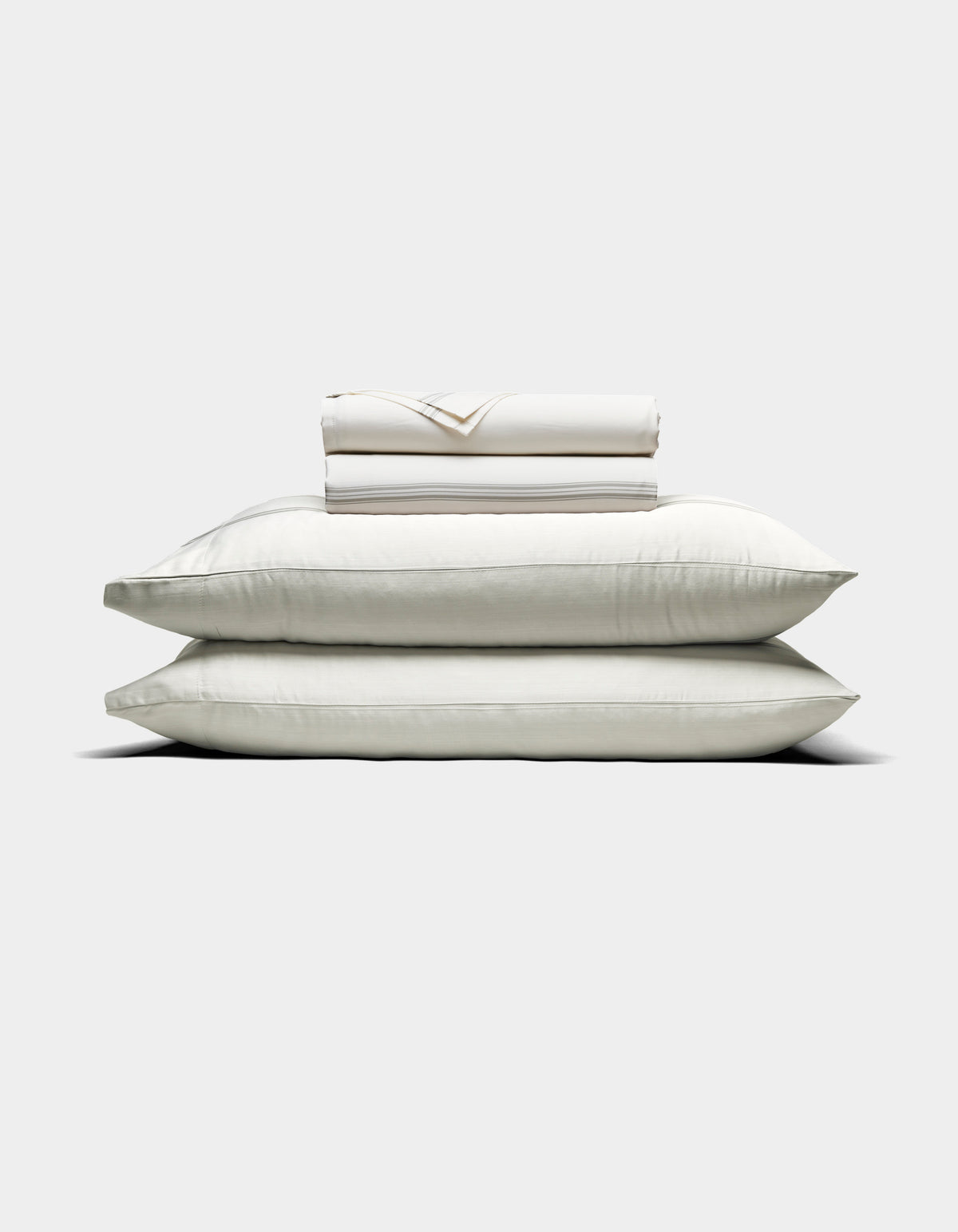 Two large white pillows are stacked with a folded Cozy Earth Bamboo Sheet Set and pillowcases placed on top, all arranged against a plain light background.