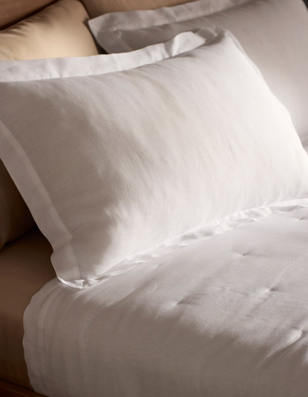 Close-up of a neatly made bed with Cozy Earth Linen Shams in white, showcasing their smooth, crisp texture. The bed features a beige headboard and looks soft and inviting.