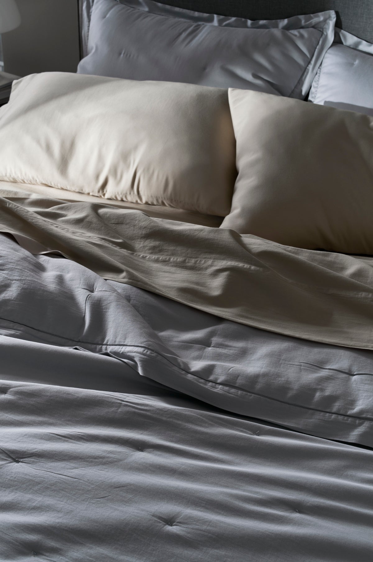 A close-up of an unmade bed features the Cozy Earth Soft-Wash Cotton Quilt with light-colored sheets and two cream pillows, creating a cozy and relaxed vibe with its gently rumpled appearance.