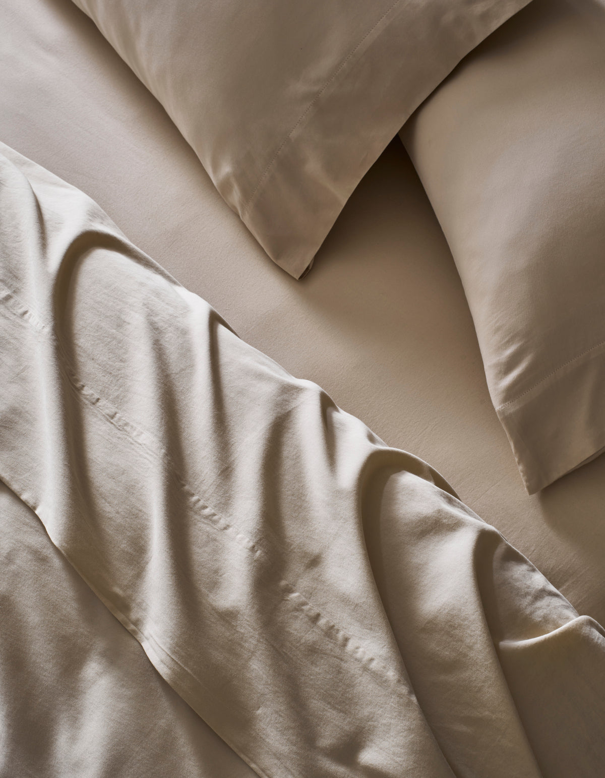 A close-up of a neatly made bed with Cozy Earth’s Soft-Wash Cotton Bedding Core Bundle, featuring beige sheets, matching pillowcases, and a slightly rumpled flat sheet over the fitted sheet and pillows.