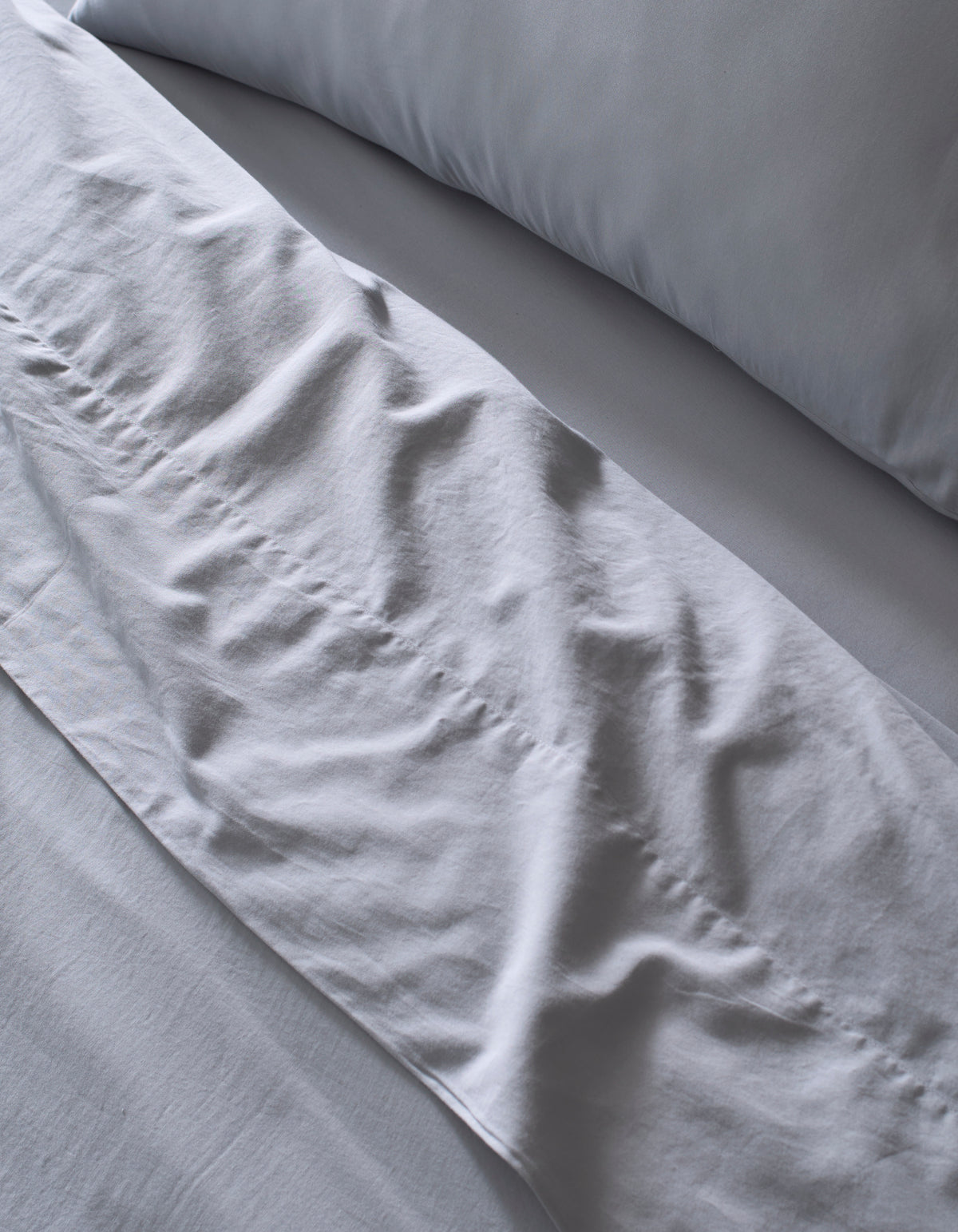 Close-up of a neatly made bed featuring the Cozy Earth Soft-Wash Cotton Bedding Core Bundle in light gray, with softly wrinkled sheets and pillowcase hinting at recent use or adjustment.