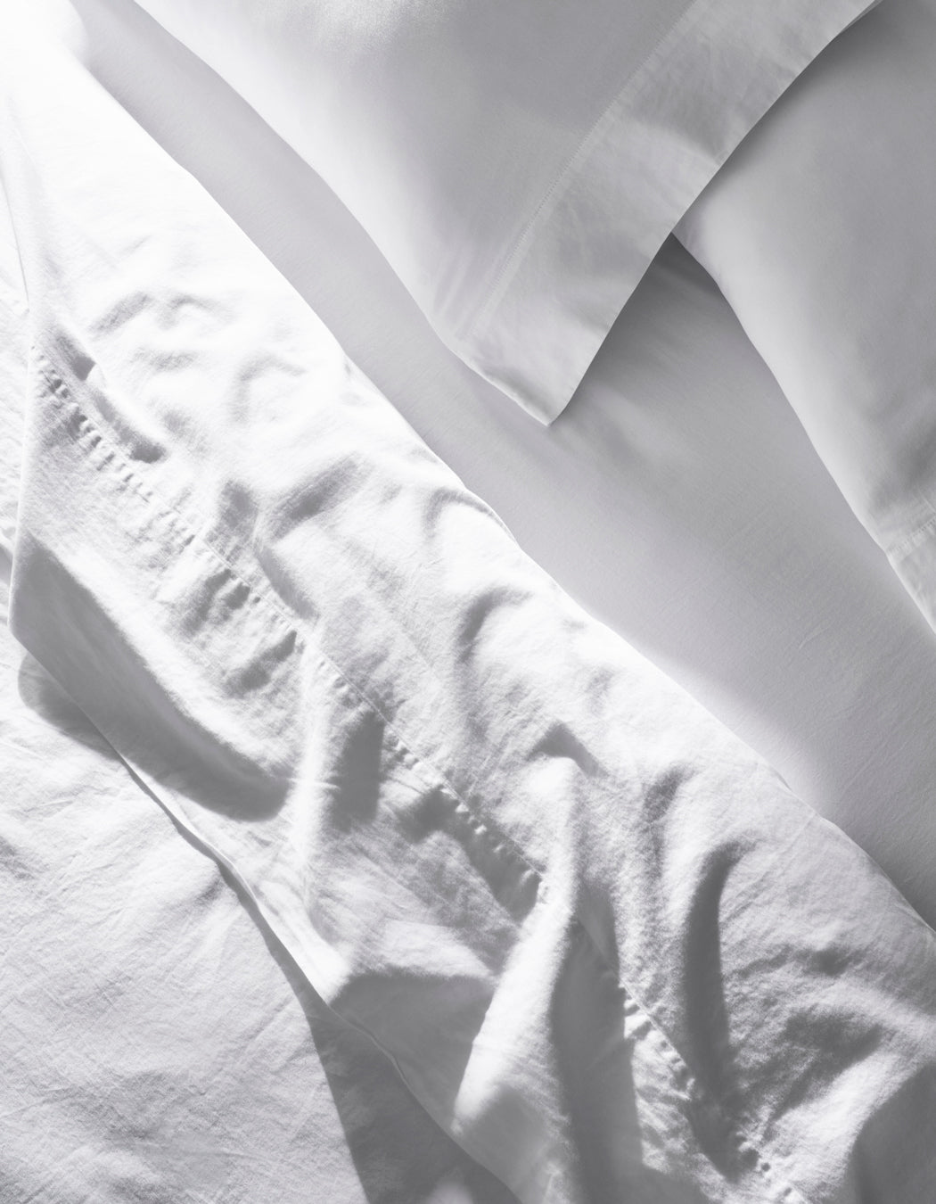The Soft-Wash Cotton Sheet Set by Cozy Earth features slightly wrinkled white bed sheets and pillowcases neatly arranged on a bed, giving a clean, bright look in natural light.