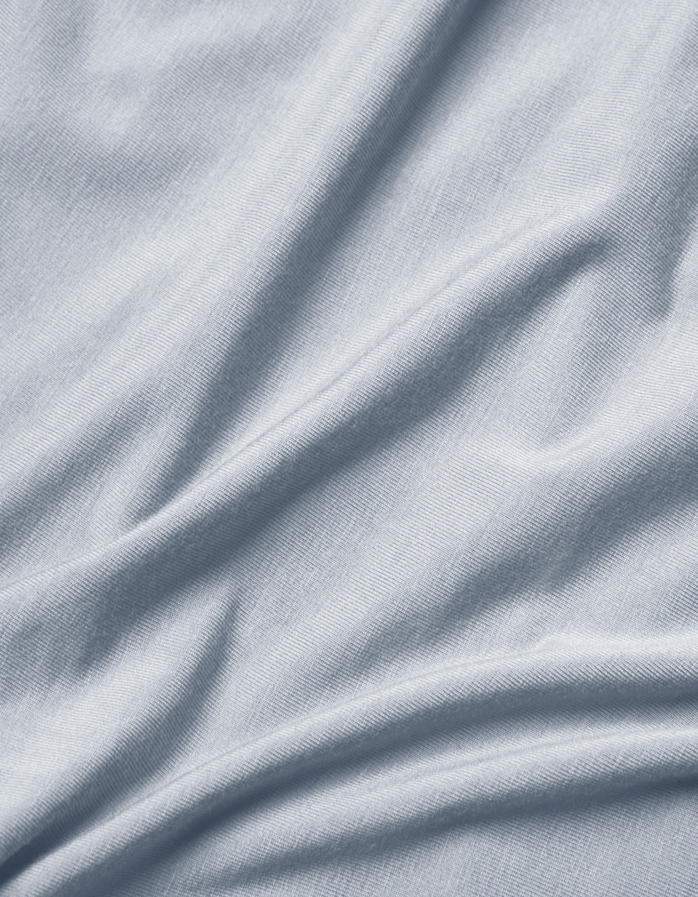 Close-up of Cozy Earth Bamboo Jersey Flat Sheet in light grey or pale blue, featuring soft folds, subtle texture, and gentle shadows and highlights.