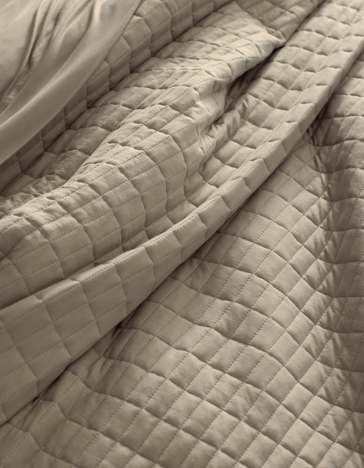 A close-up of the Cozy Earth Bamboo Jersey Quilt in beige, featuring a soft, quilted square pattern with gentle folds and visible texture.