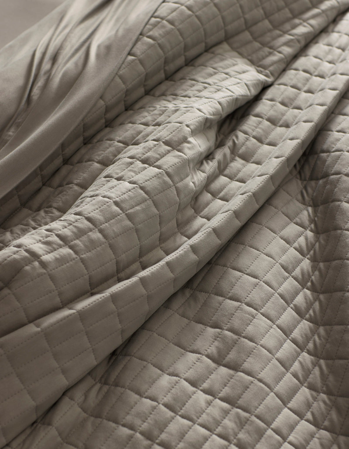 Close-up of the Cozy Earth Bamboo Jersey Quilt in light gray, featuring a quilted grid pattern with visible folds and soft texture for a cozy, inviting look.|Color:Stone