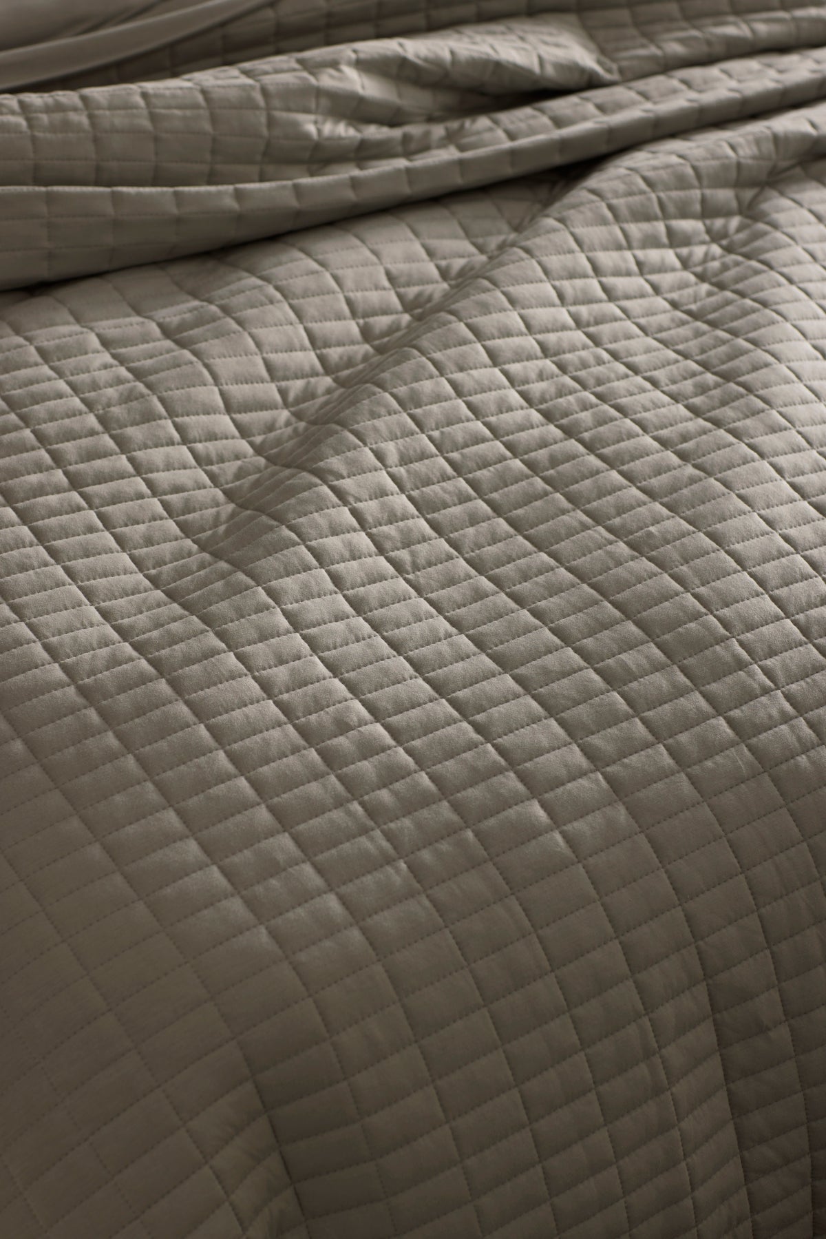Close-up of a neatly made bed with the Cozy Earth Bamboo Jersey Quilt Bundle, featuring a soft, slightly wrinkled quilt in a light neutral tone with a grid of stitched squares.