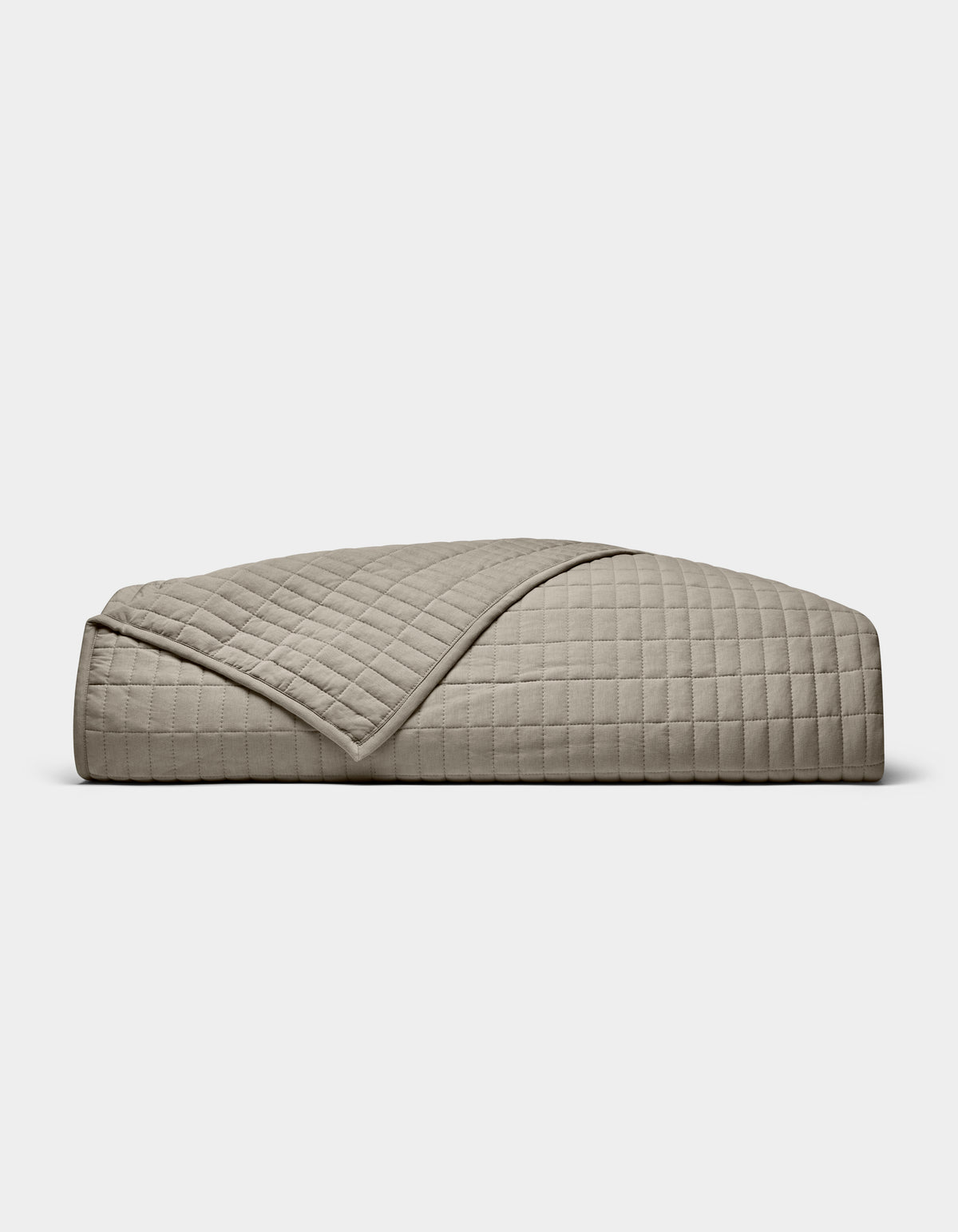 The Cozy Earth Bamboo Jersey Quilt is shown folded against a white background, with one corner turned down to display its beige color, grid pattern, and detailed stitching.