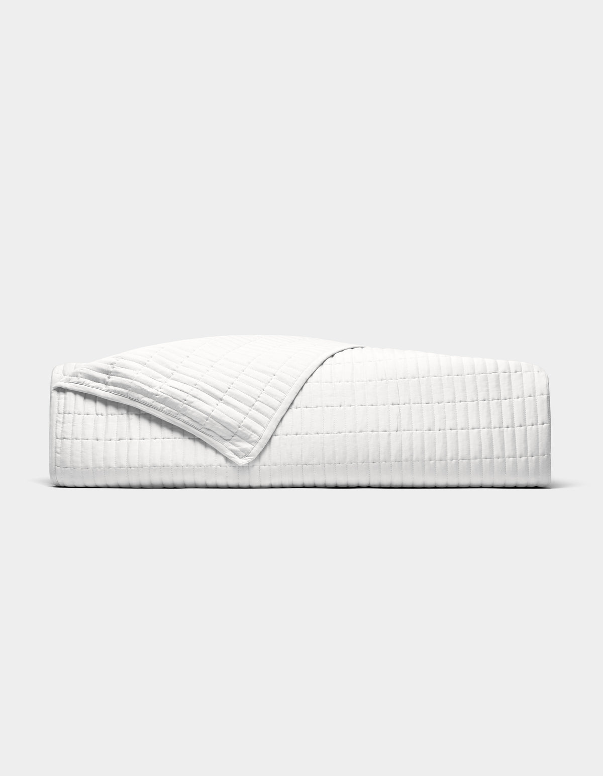 The Cozy Earth Bamboo Jersey Quilt is shown neatly made on a bed, its white, textured fabric partially folded back, photographed from the side against a plain light grey background.