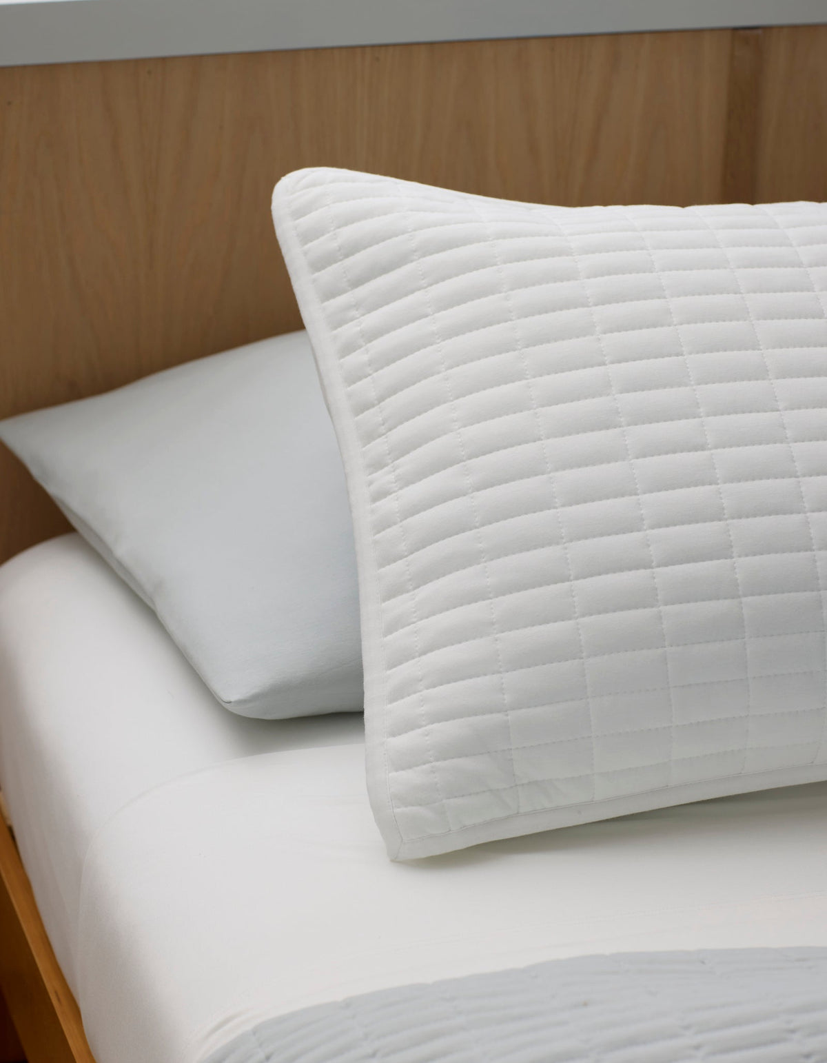 The Bamboo Jersey Quilt Bundle by Cozy Earth features a front pillow with a white, quilted grid cover and a back pillow in plain light gray, styled on a neatly made bed with a simple, minimalist aesthetic.