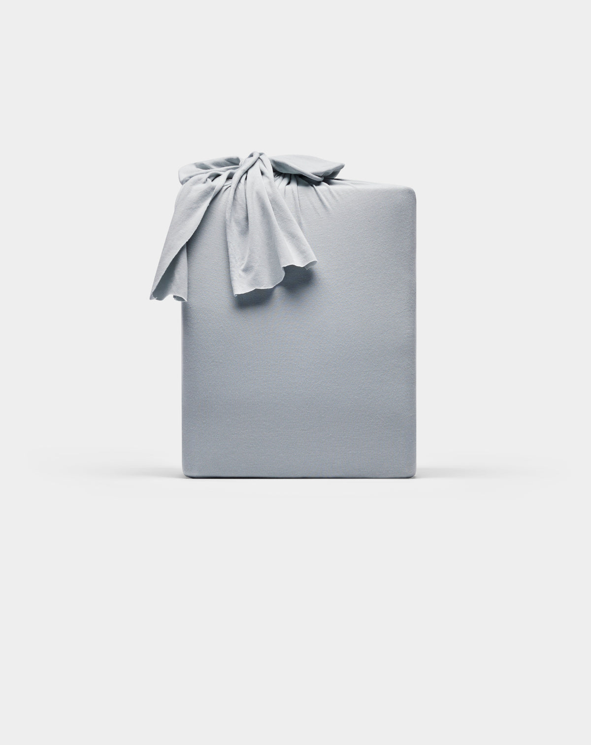 A rectangular Bamboo Jersey Sheet Set by Cozy Earth, wrapped in smooth, light gray fabric with a knot on top, displayed against a plain white background.