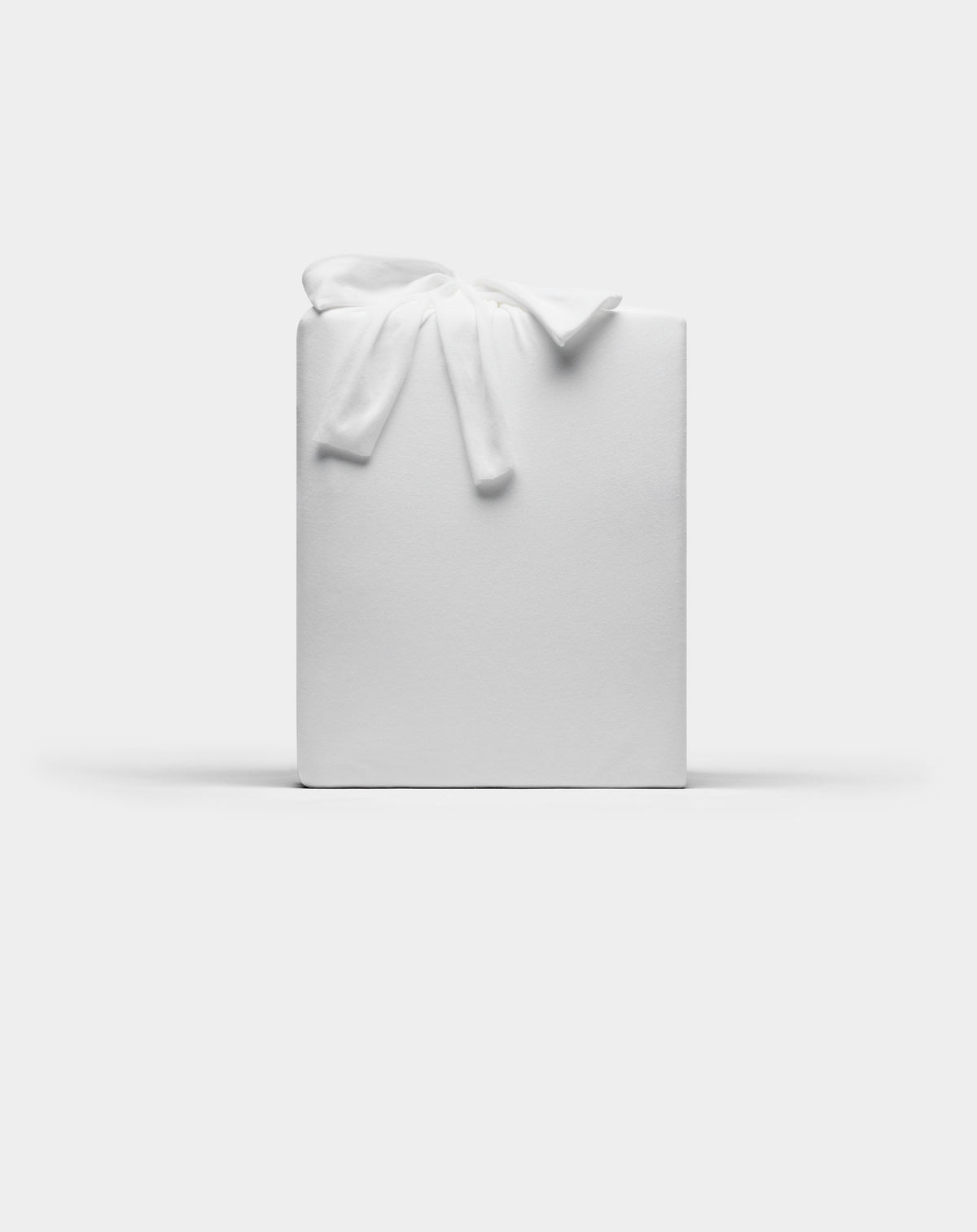 A Bamboo Jersey Sheet Set by Cozy Earth, wrapped in plain white paper with a white fabric bow on top, set against a plain white background.