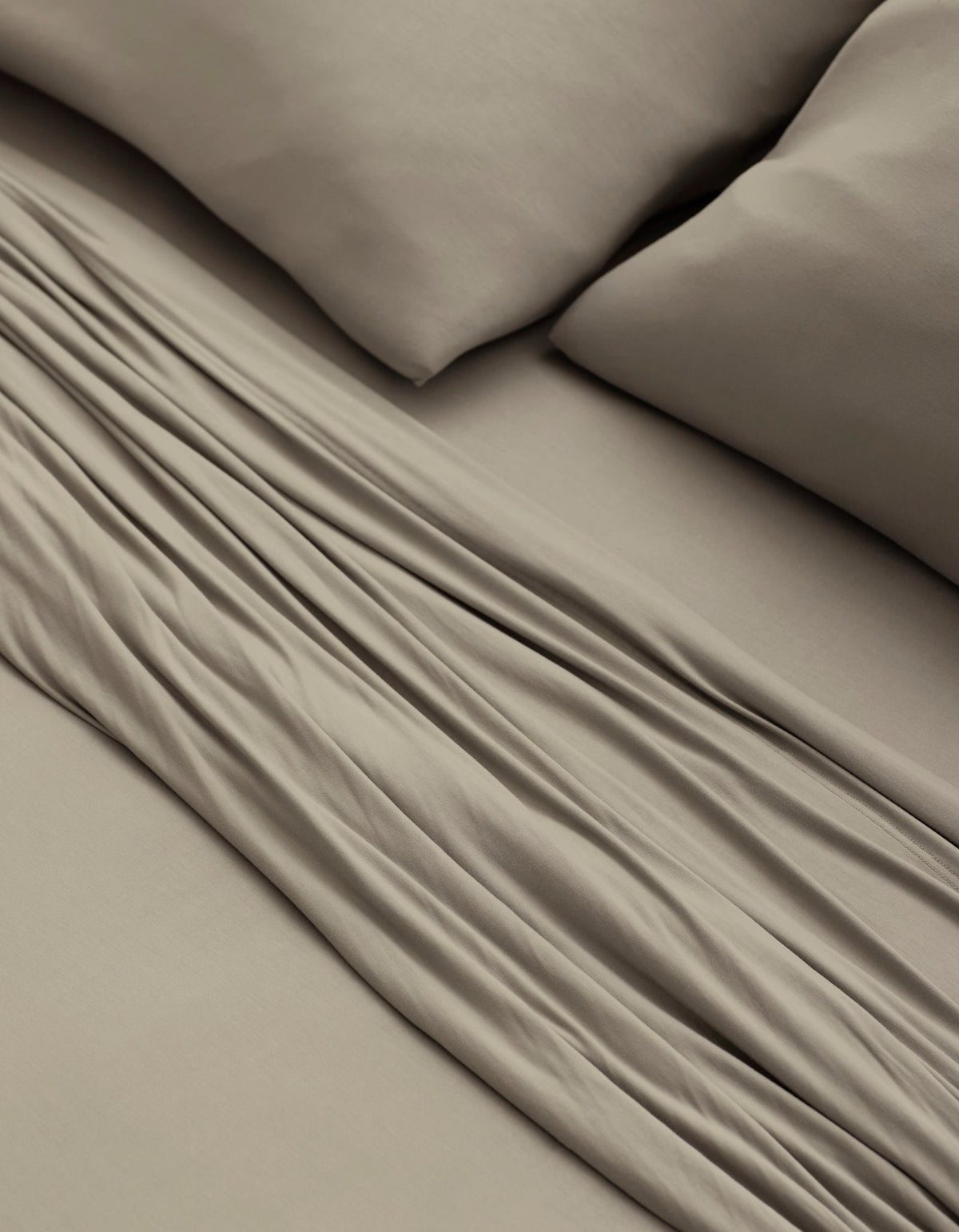 A close-up of a bed made with Cozy Earth’s Bamboo Jersey Sheet Set in taupe, featuring two matching pillows and showcasing the soft fabric folds and smooth texture.