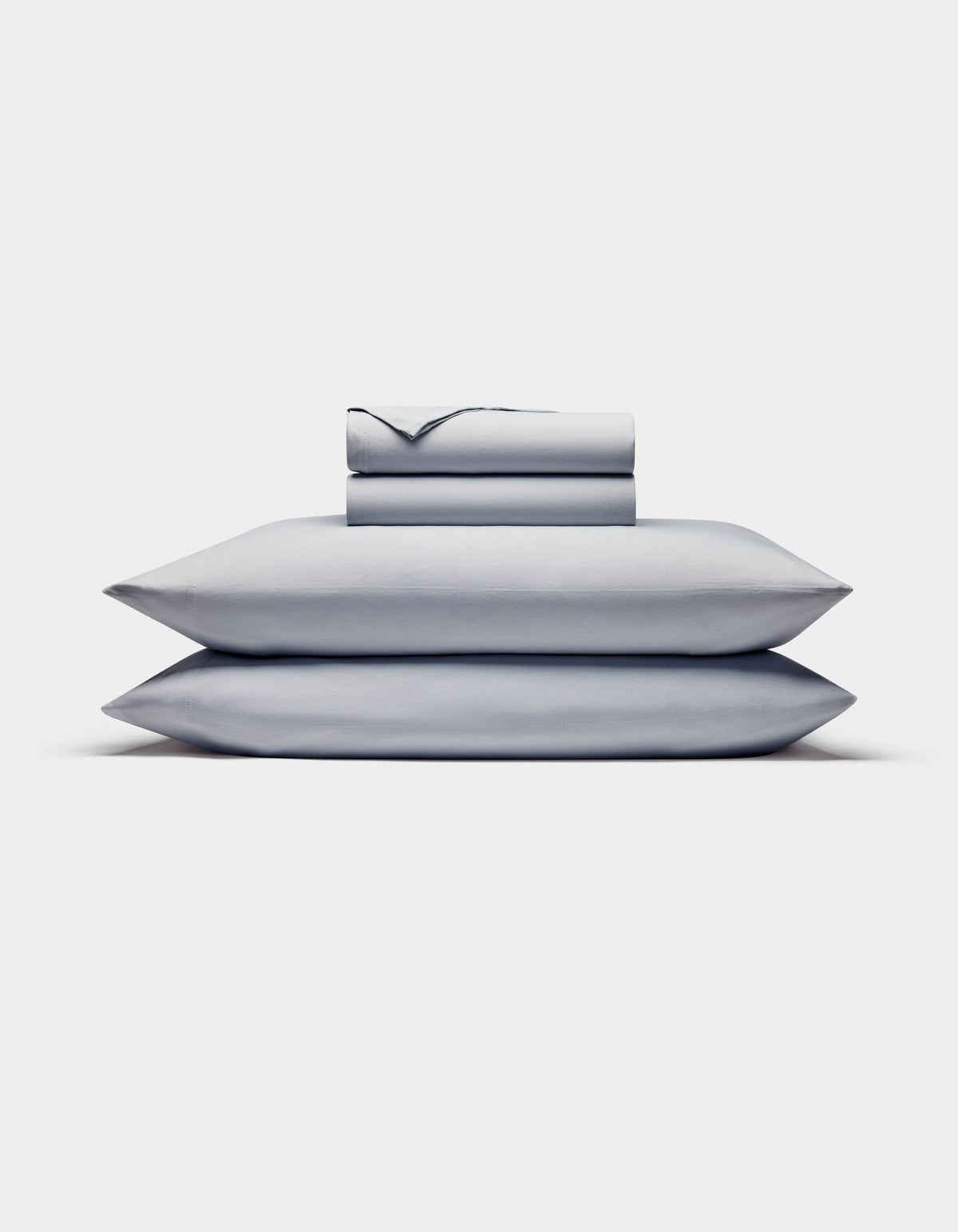 The Cozy Earth Bamboo Jersey Sheet Set is shown neatly stacked with two pillows at the bottom and folded light gray sheets and pillowcases on top, all set against a plain white background.