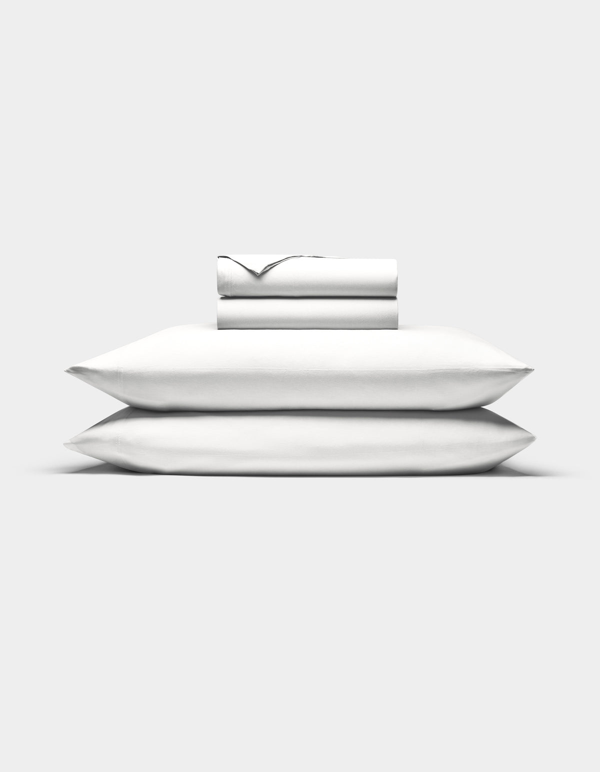 Two white Cozy Earth Bamboo Jersey Sheet Set sheets are neatly folded atop two stacked pillows, all set against a plain white background.|Color:White