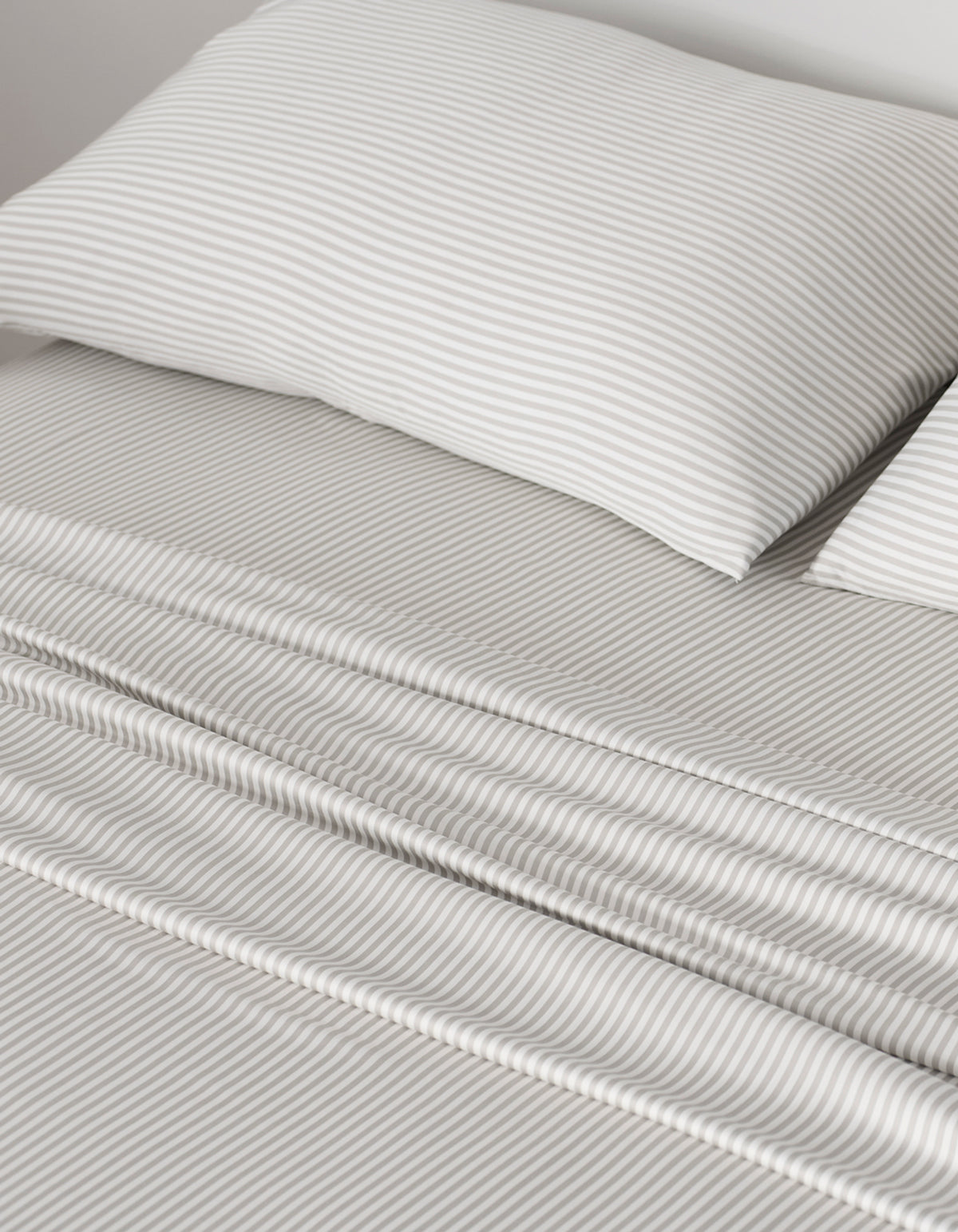 A neatly made bed showcases Cozy Earth Bamboo Pillowcases and sheets with thin, light gray and white horizontal stripes, giving the bedding a smooth, clean look that creates a calm and cozy atmosphere.