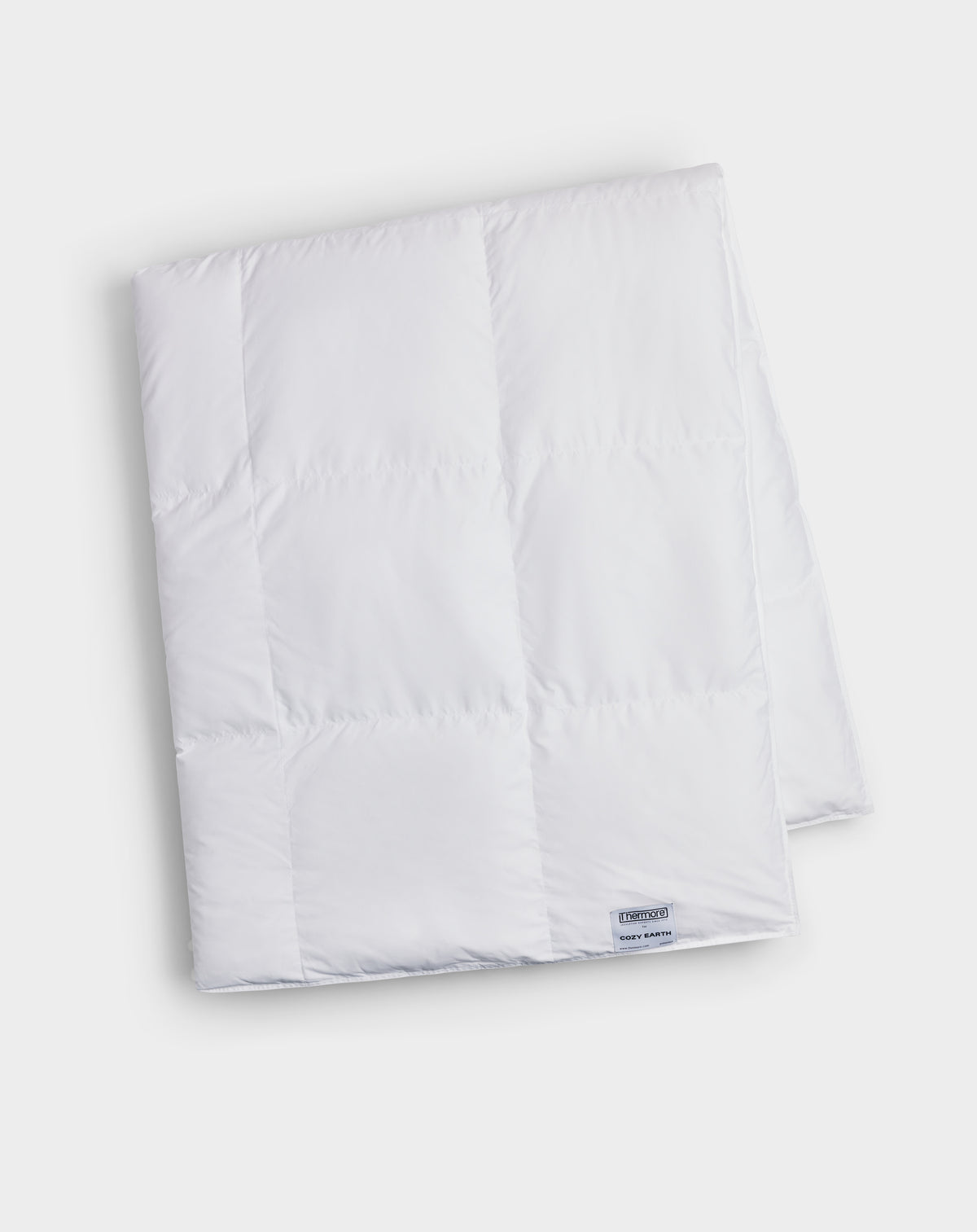 The Cozy Earth Down Alternative Throw, in white with stitched squares and a small corner label, is neatly folded and displayed on a plain light background.