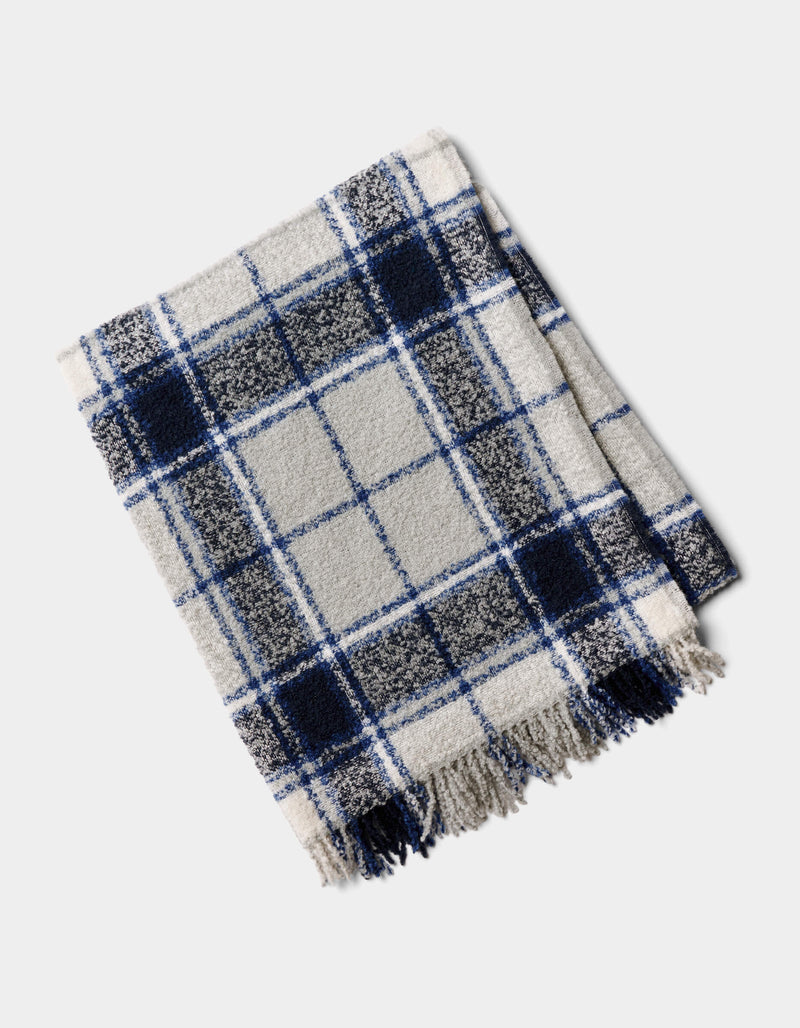 The Cozy Earth Alpaca Boucle Throw, featuring a blue, black, and white plaid design with fringed edges, is shown folded on a light background.