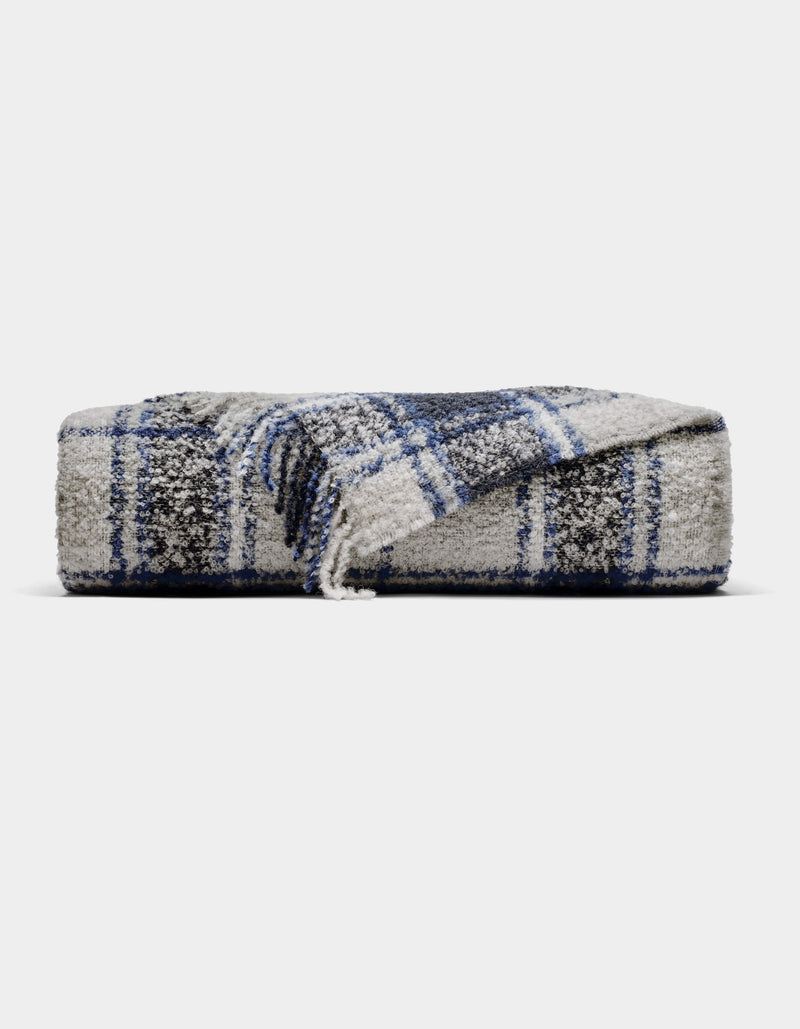 The Cozy Earth Alpaca Boucle Throw is a soft, gray blanket with a blue and white plaid pattern. Displayed against a plain background, one corner is partially unfolded to showcase its unique texture and design.