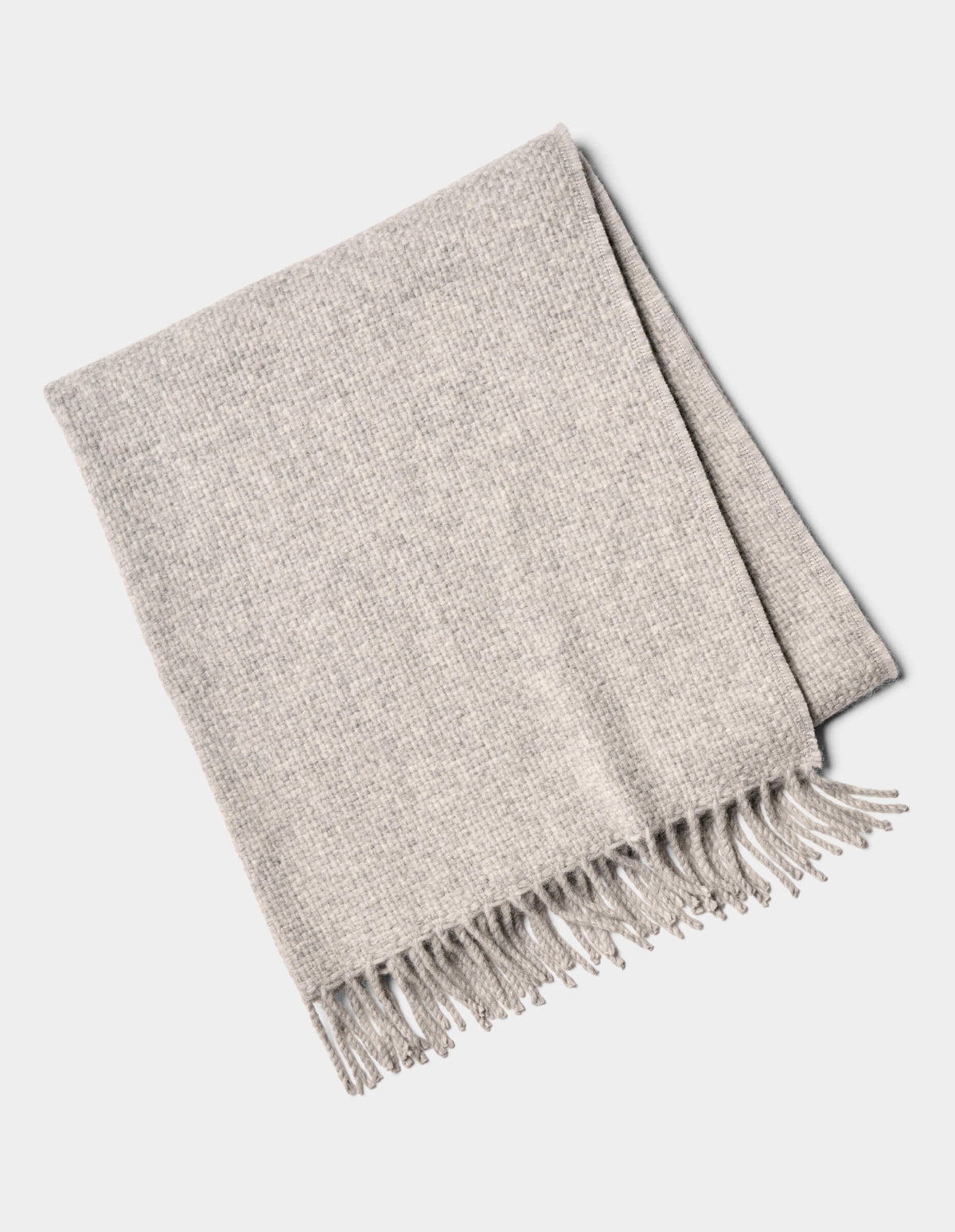 The Lucia Throw by Cozy Earth is a folded light gray woven blanket with fringe on one side, shown on a white background.