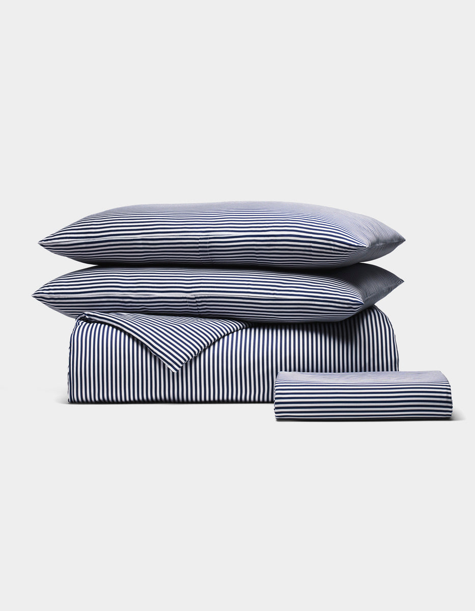 The Cozy Earth Bamboo Bedding Essential Bundle, featuring two pillows, a duvet, and a folded sheet in blue and white stripes, is neatly stacked on a plain white background.