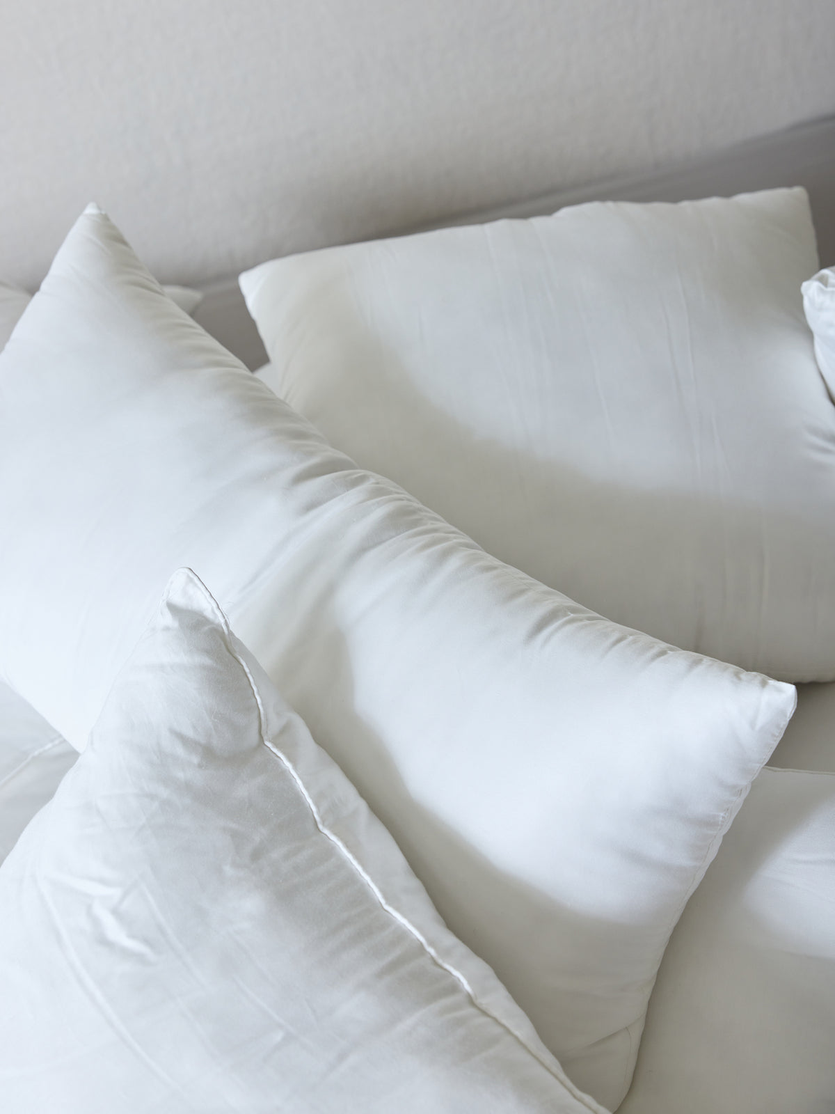 A close-up view of several **Cozy Earth Premium Down Alternative Inserts** arranged on a bed with white sheets. The pillows, varying slightly in shape and size, create a soft and cozy atmosphere. The background features a muted light color, enhancing the serene and clean setting. 