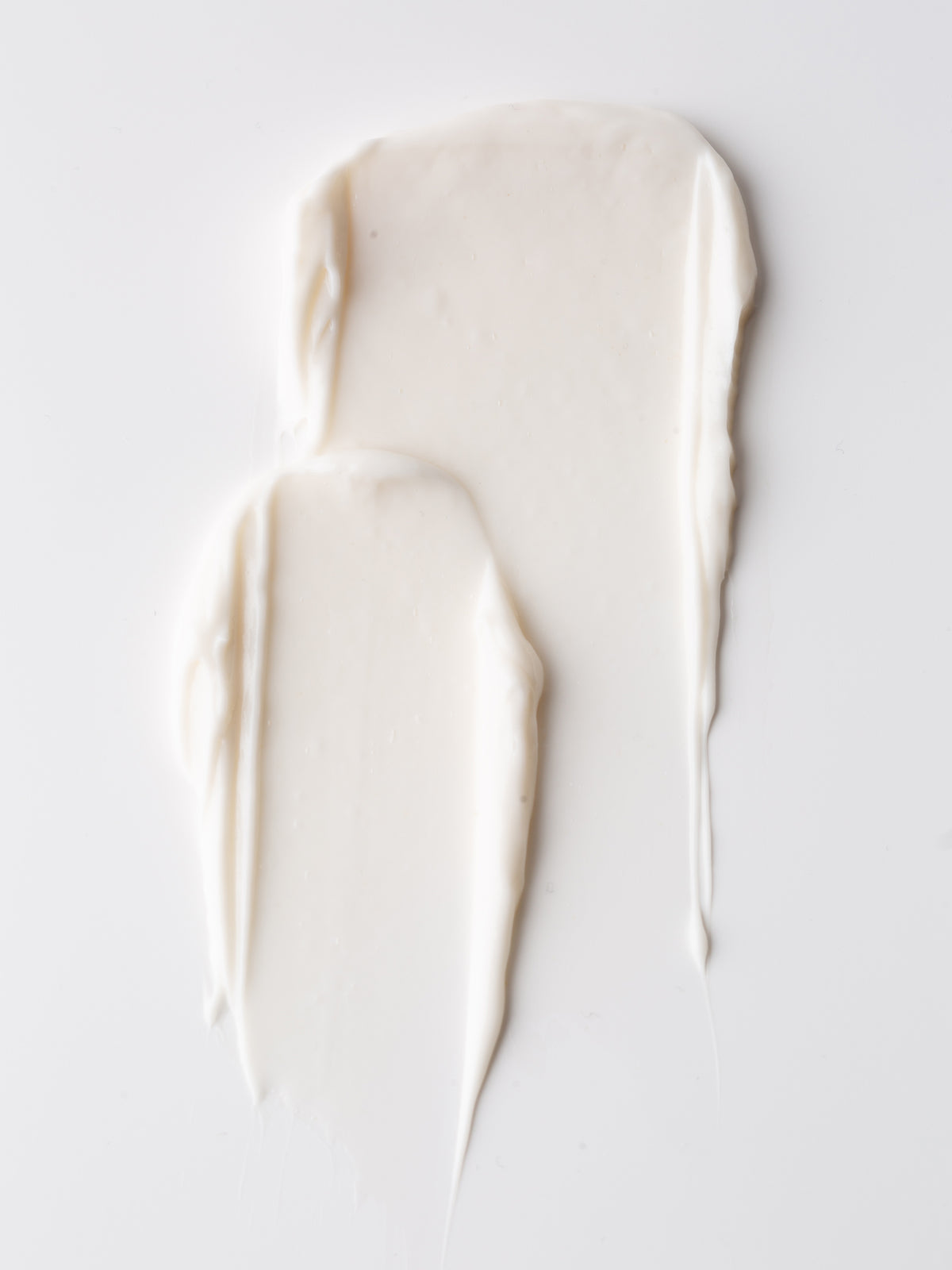 Two swipes of Fount Society Intro Kit moisturizer by Cozy Earth are smeared on a smooth white surface, creating soft, textured, elongated shapes.