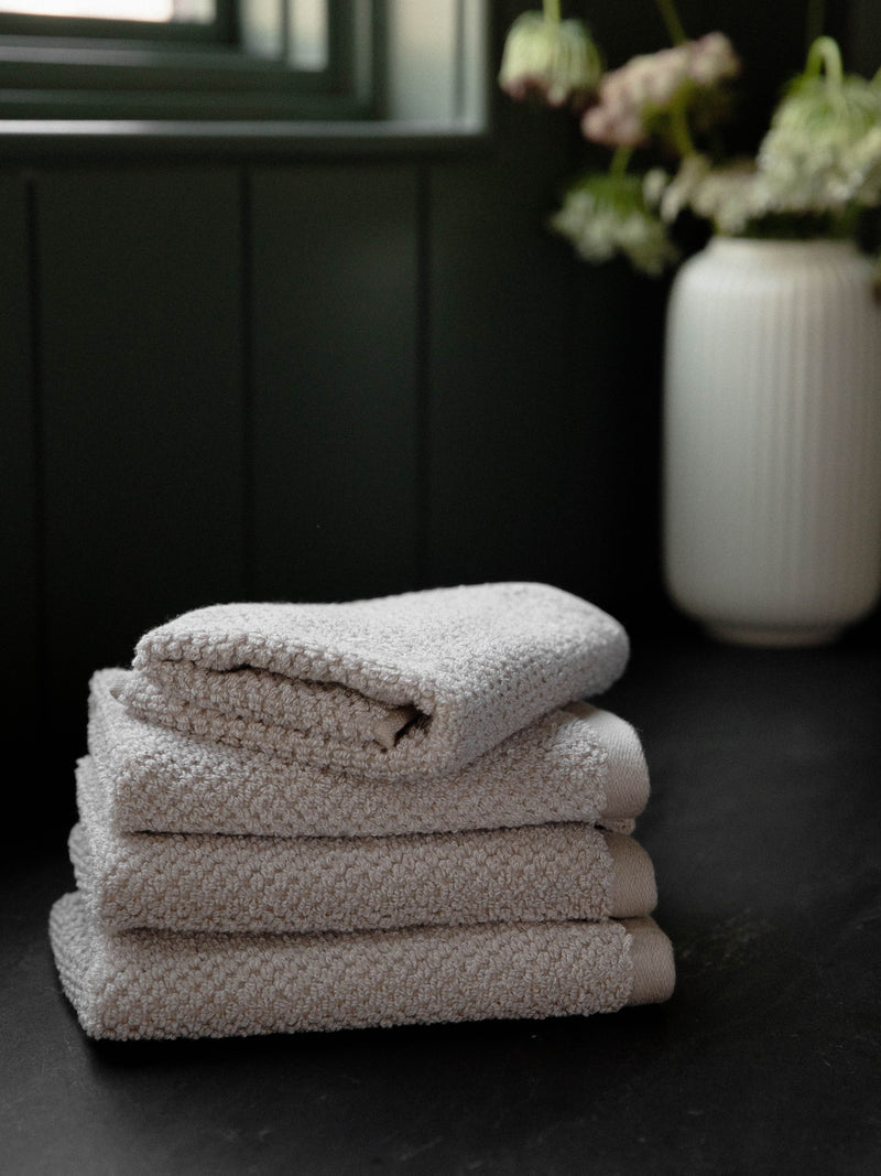 Nantucket Wash Cloths in the color Heathered Sand. Photo of Nantucket Wash Cloths taken with the Wash Cloths resting on a countertop in a bathroom.