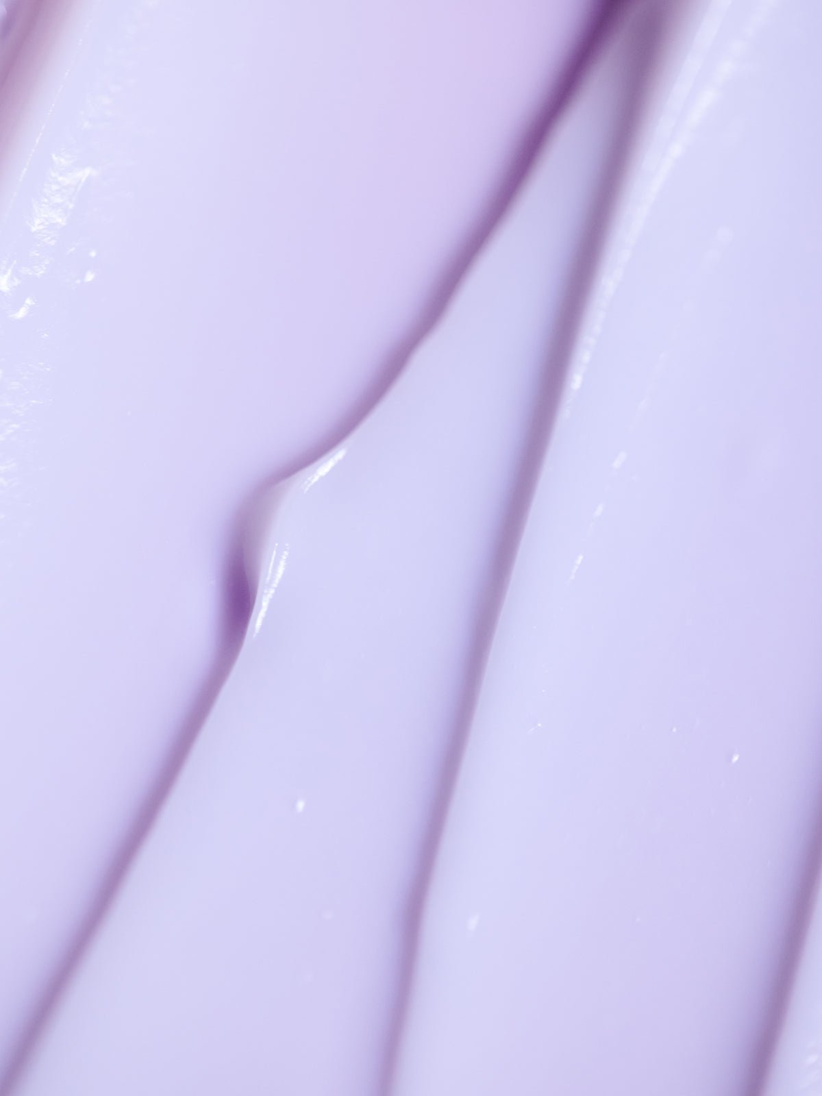 Close-up of Cozy Earth's Night Cream, showcasing its smooth purple texture with light reflections forming an abstract pattern of creamy ridges and folds. 