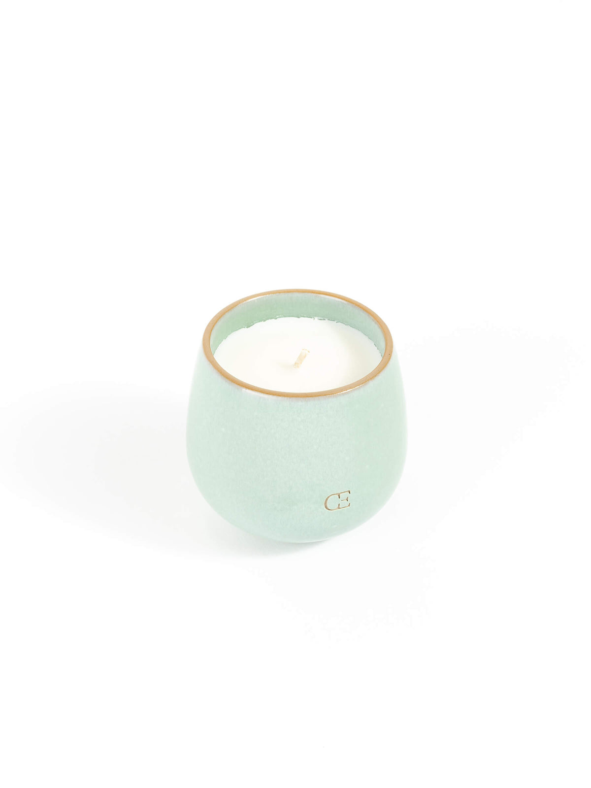 The Cozy Earth Candle UNWIND is a small, round, light green ceramic holder with a white candle inside, shown against a plain white background.