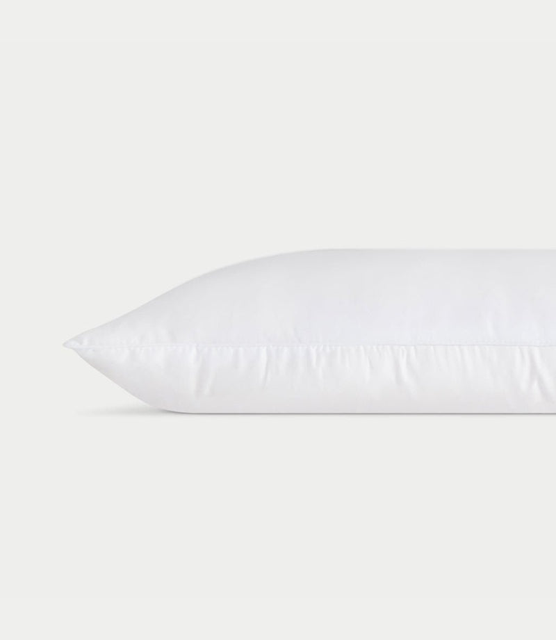 A white **Silk Pillow** from **Cozy Earth** lies horizontally against a plain white background, showcasing a clean and smooth surface with faint stitching along the edge, giving it a fresh and fluffy appearance.