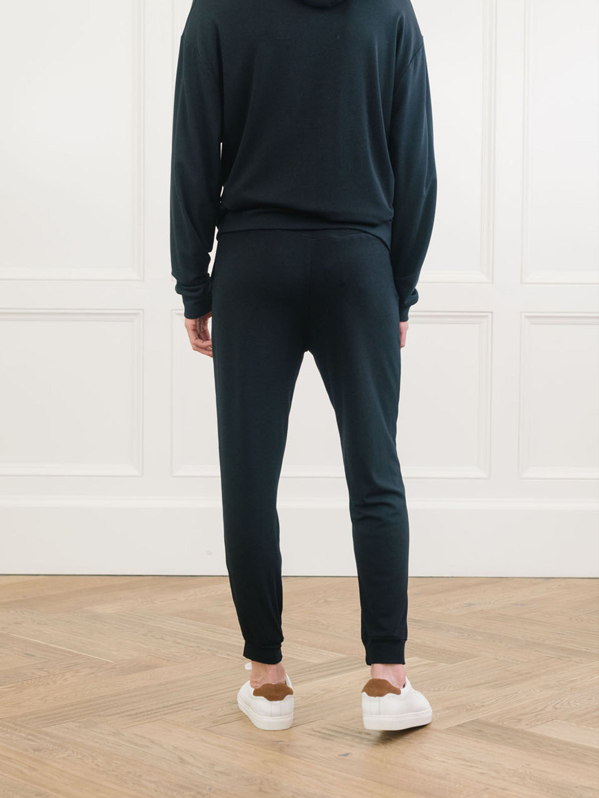 A man pictured from the waist down wears Men's Brushed Bamboo Hoodie & Jogger Set in Black. He faces away from the camera. 