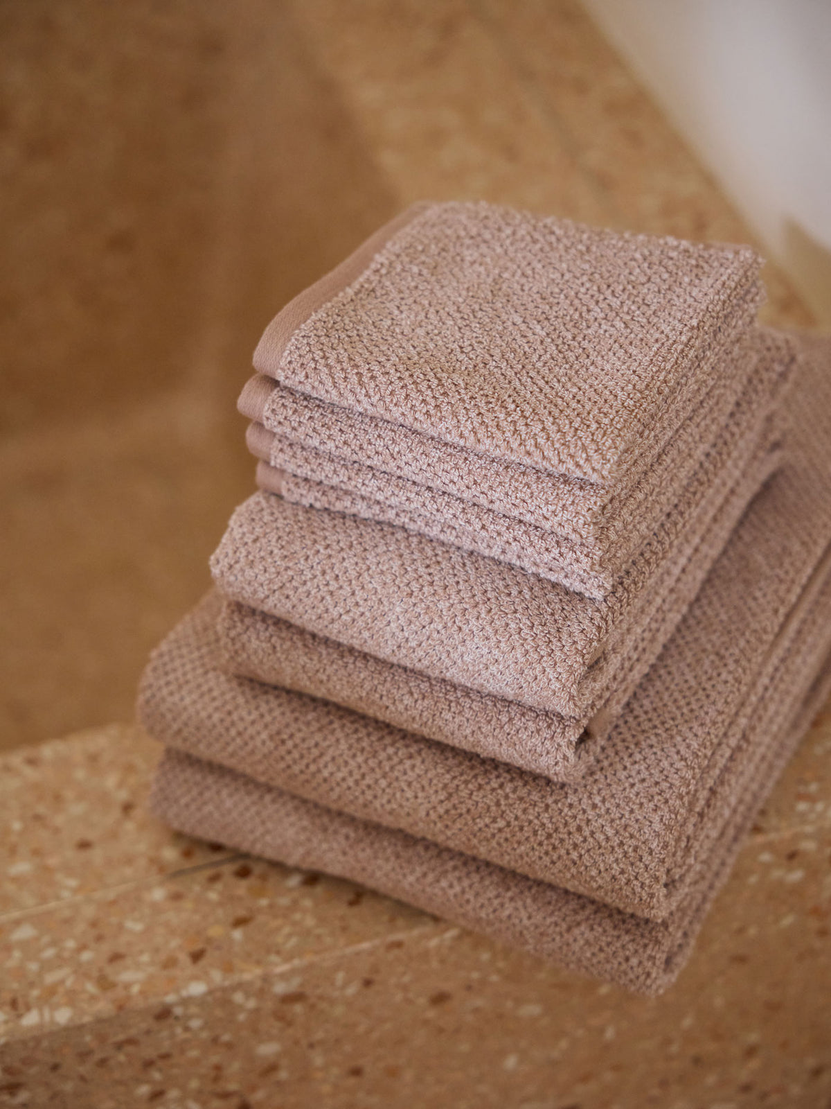 A stack of Cozy Earth bath towels sit on the edge of a stone bathtub. 